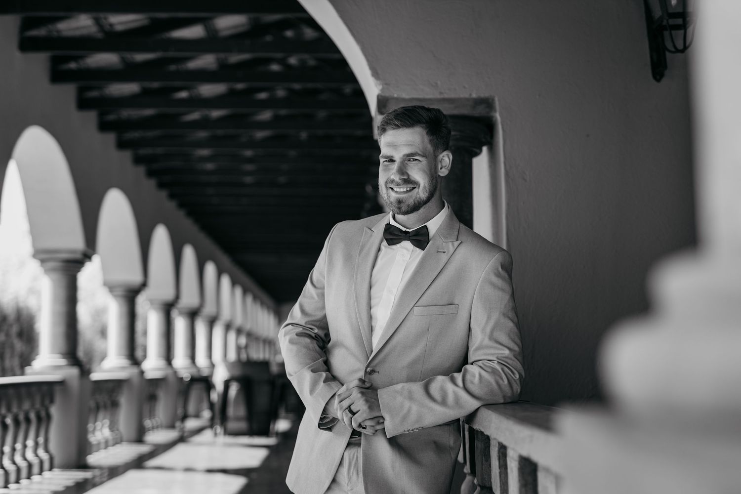 Black and white portrait of someone in formal attire standing in an arched colonnade.