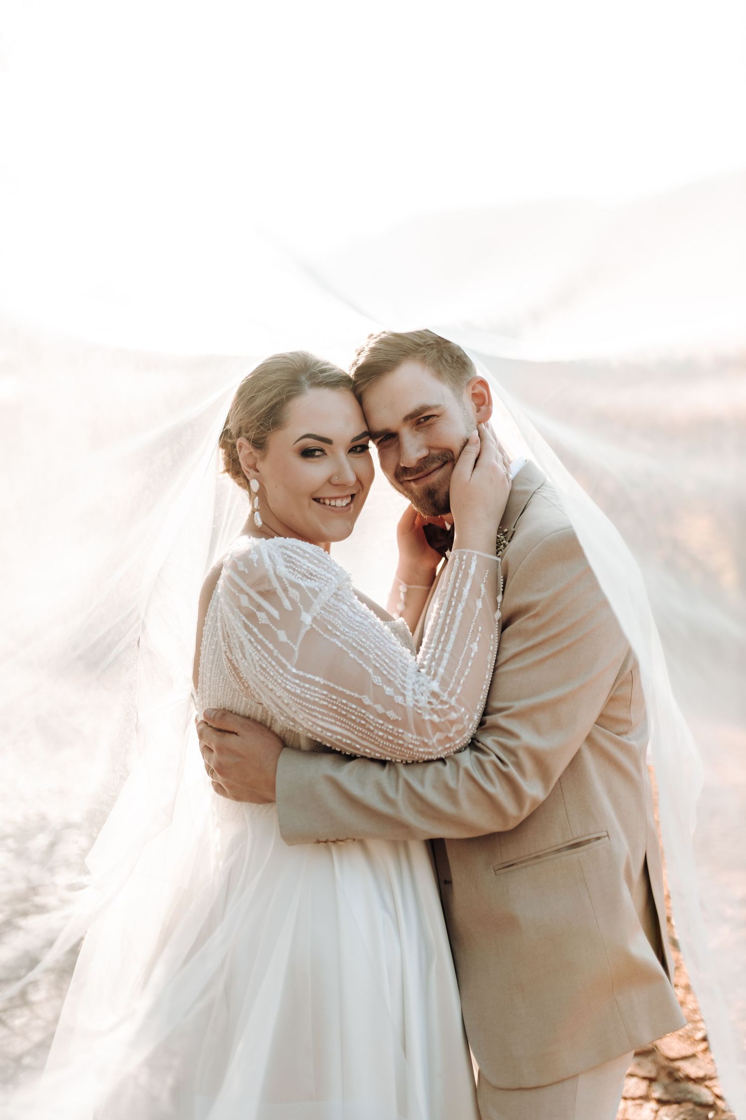 Joyful wedding portrait showing tender moment between couple with flowing veil and natural lighting.