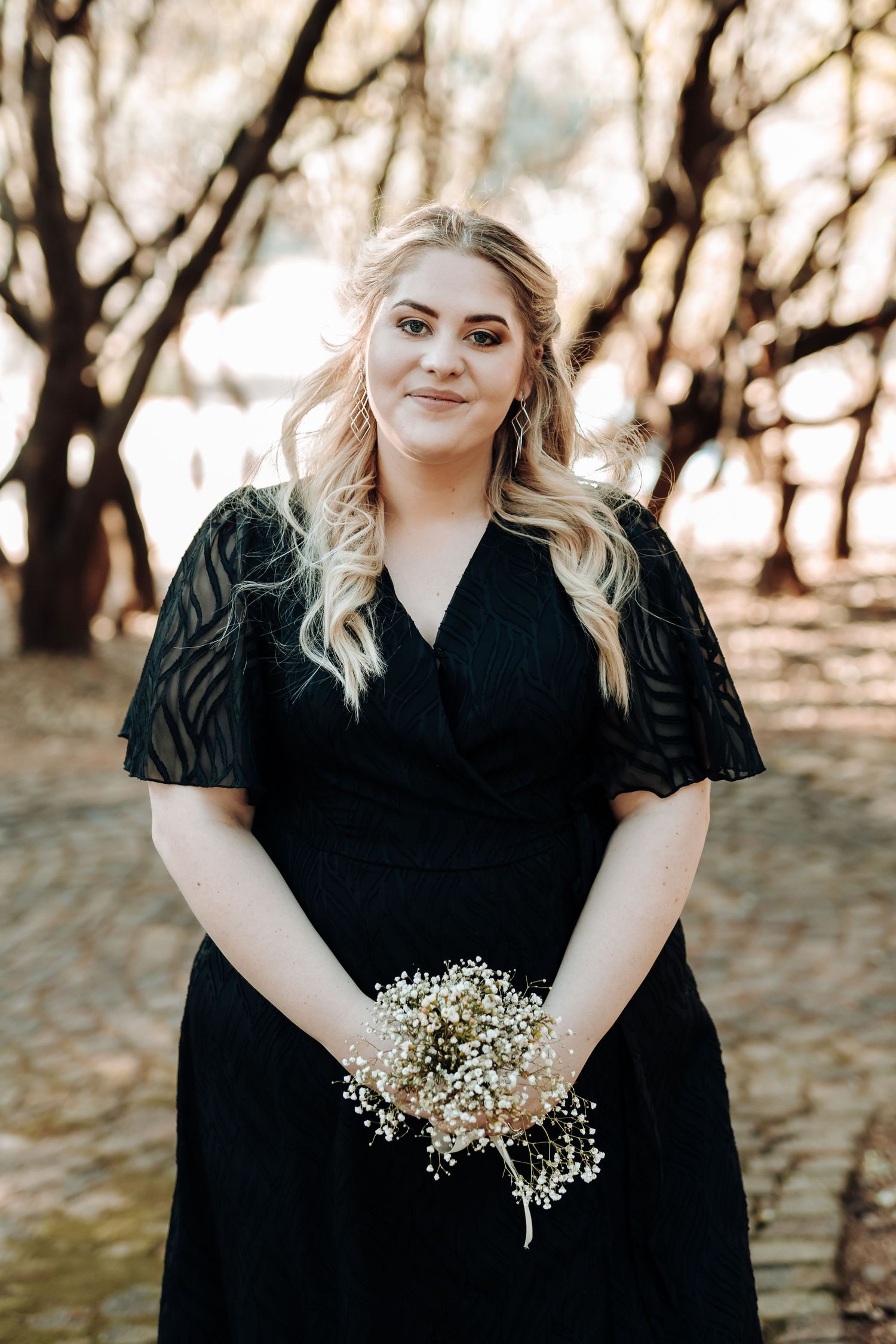 Bridesmaid in black dress with puffy sleeves holds baby's breath bouquet in outdoor setting.