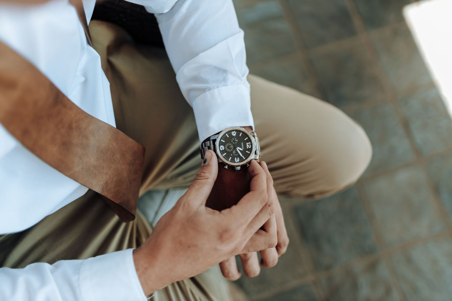 Close-up of hands adjusting an elegant wristwatch with brown leather strap.