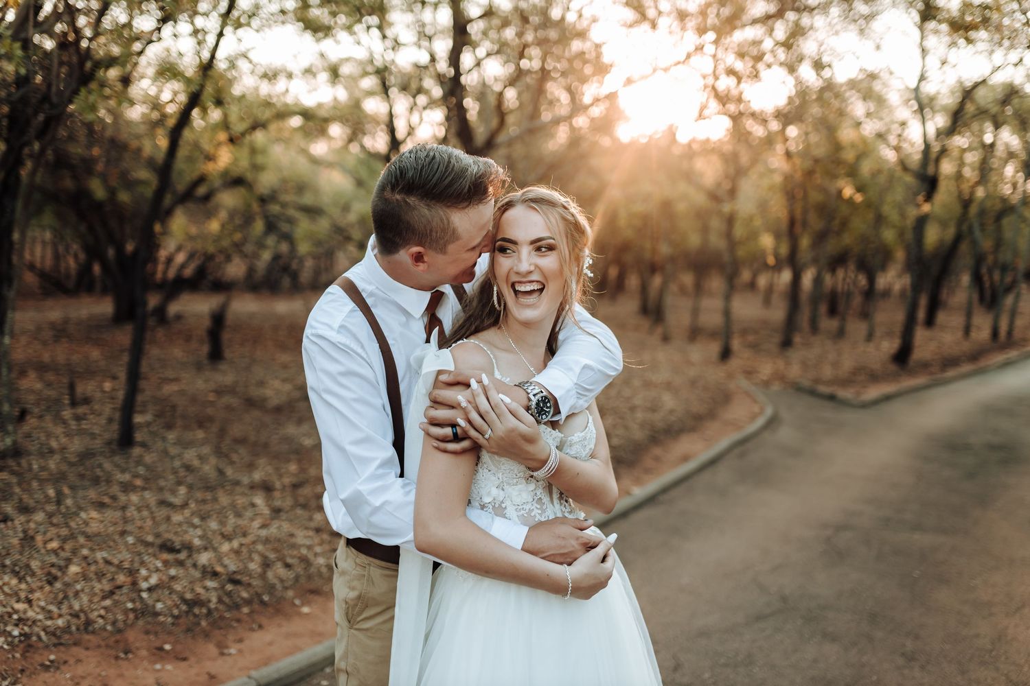 A joyful wedding moment captured on a tree-lined path at sunset.