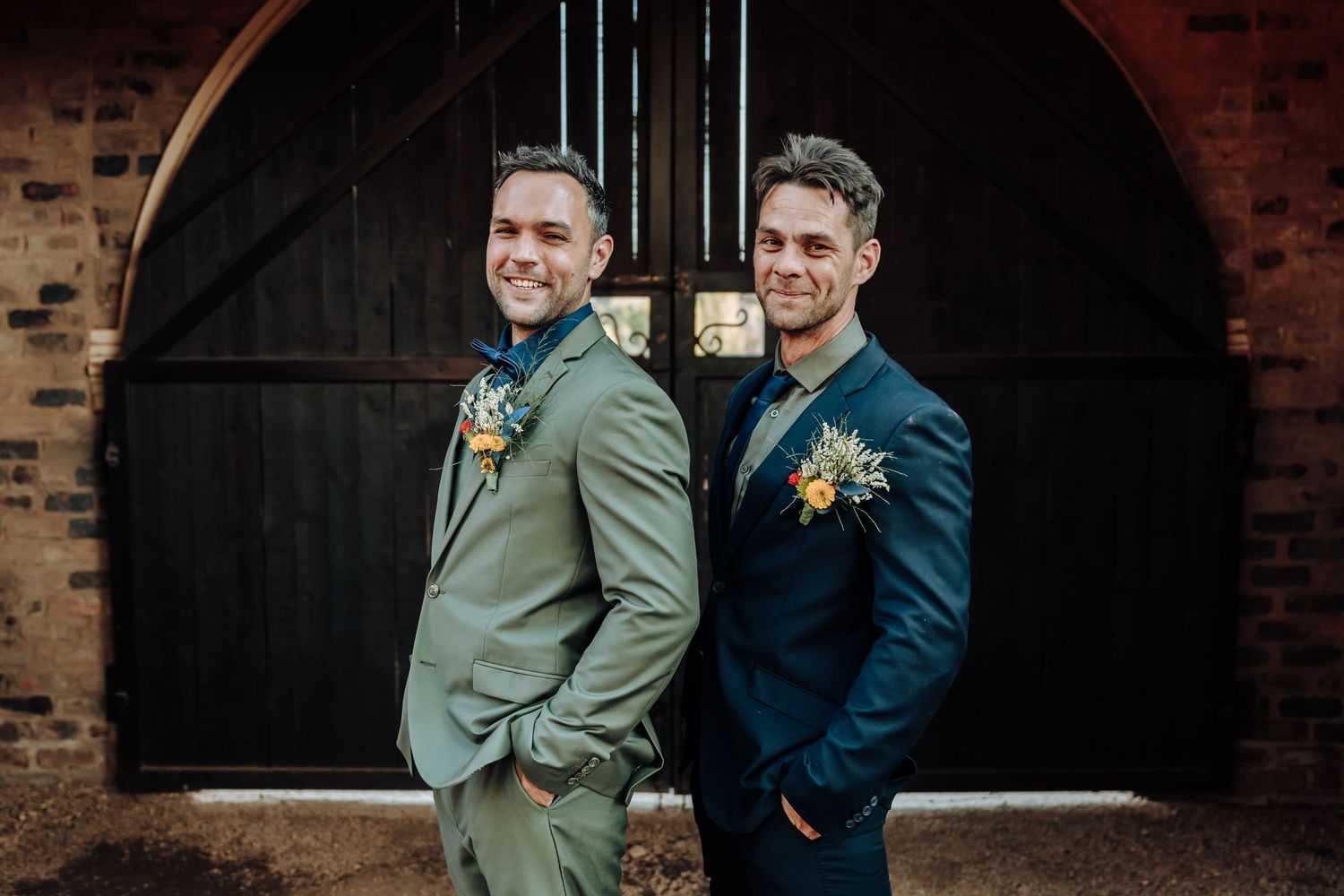 Wedding party members in complementary suits pose casually against a dark arched doorway.
