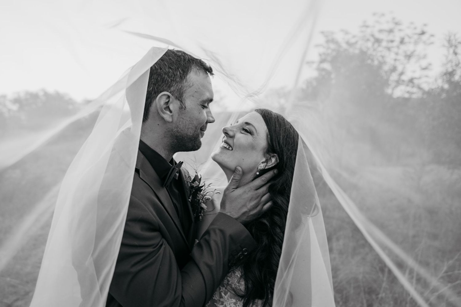 Intimate black and white portrait of newlyweds sharing a tender moment under a veil.