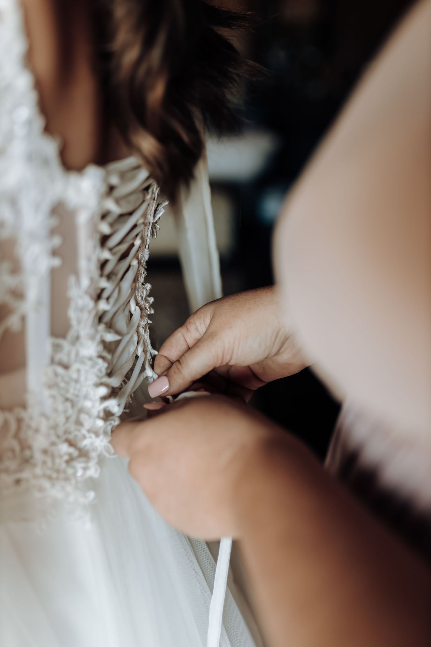 Close-up detail of hands lacing up a wedding dress corset back.