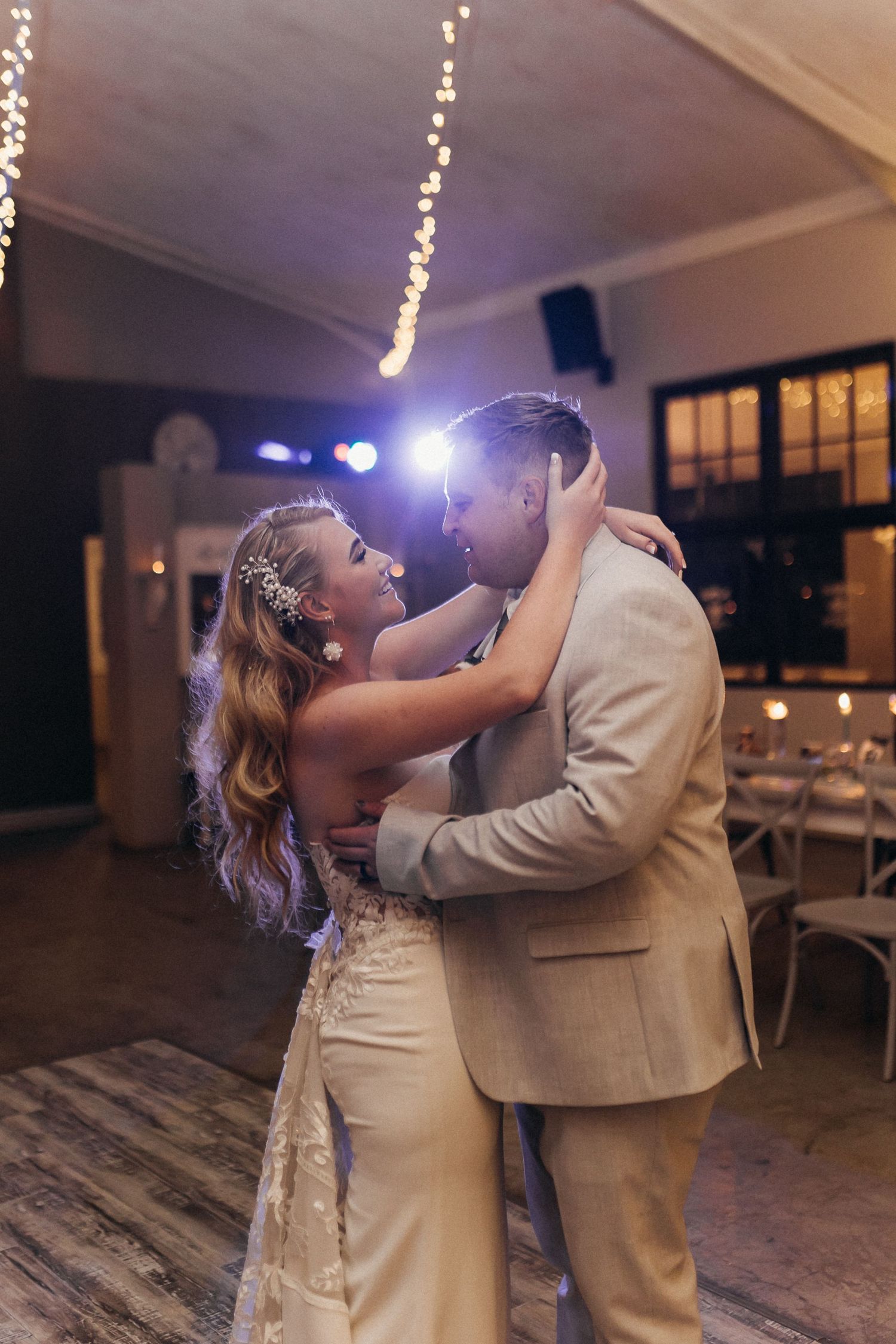 Couple sharing intimate first dance moment under twinkling lights at wedding reception.