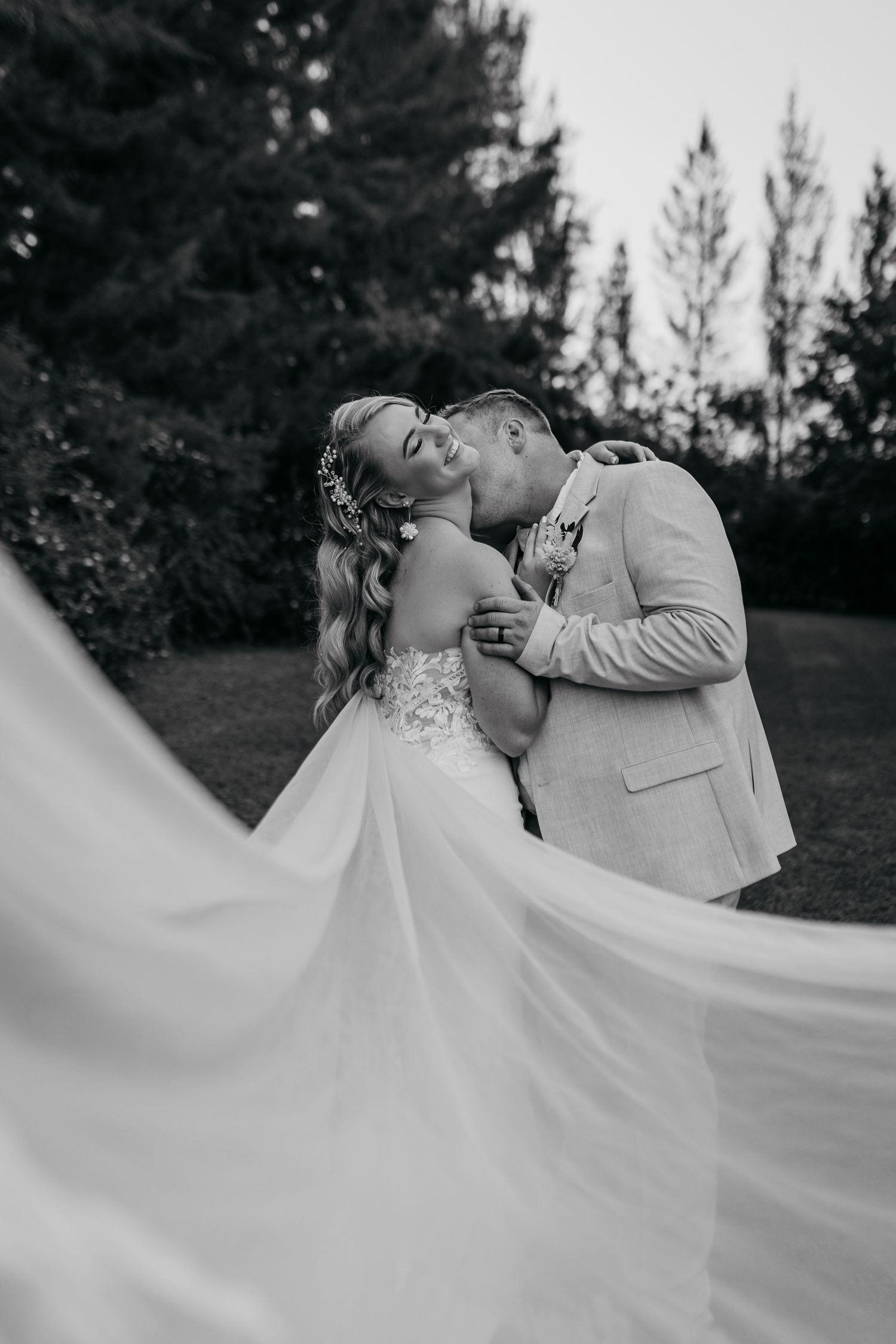 Black and white wedding portrait with dramatic flowing dress in outdoor garden setting.
