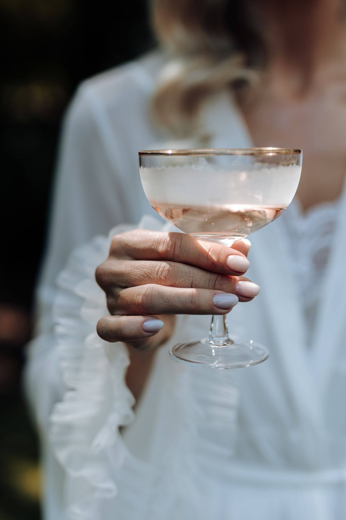 Closeup of hands holding a delicate champagne coupe glass with pink bubbly drink.