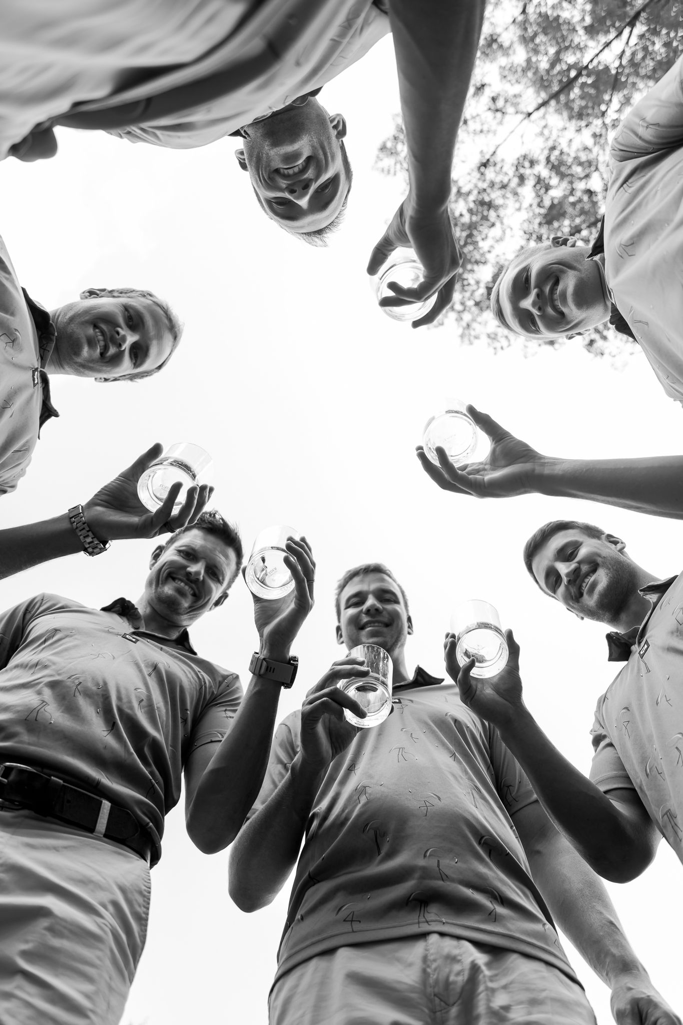 Low angle black and white shot of group forming circle against bright sky.
