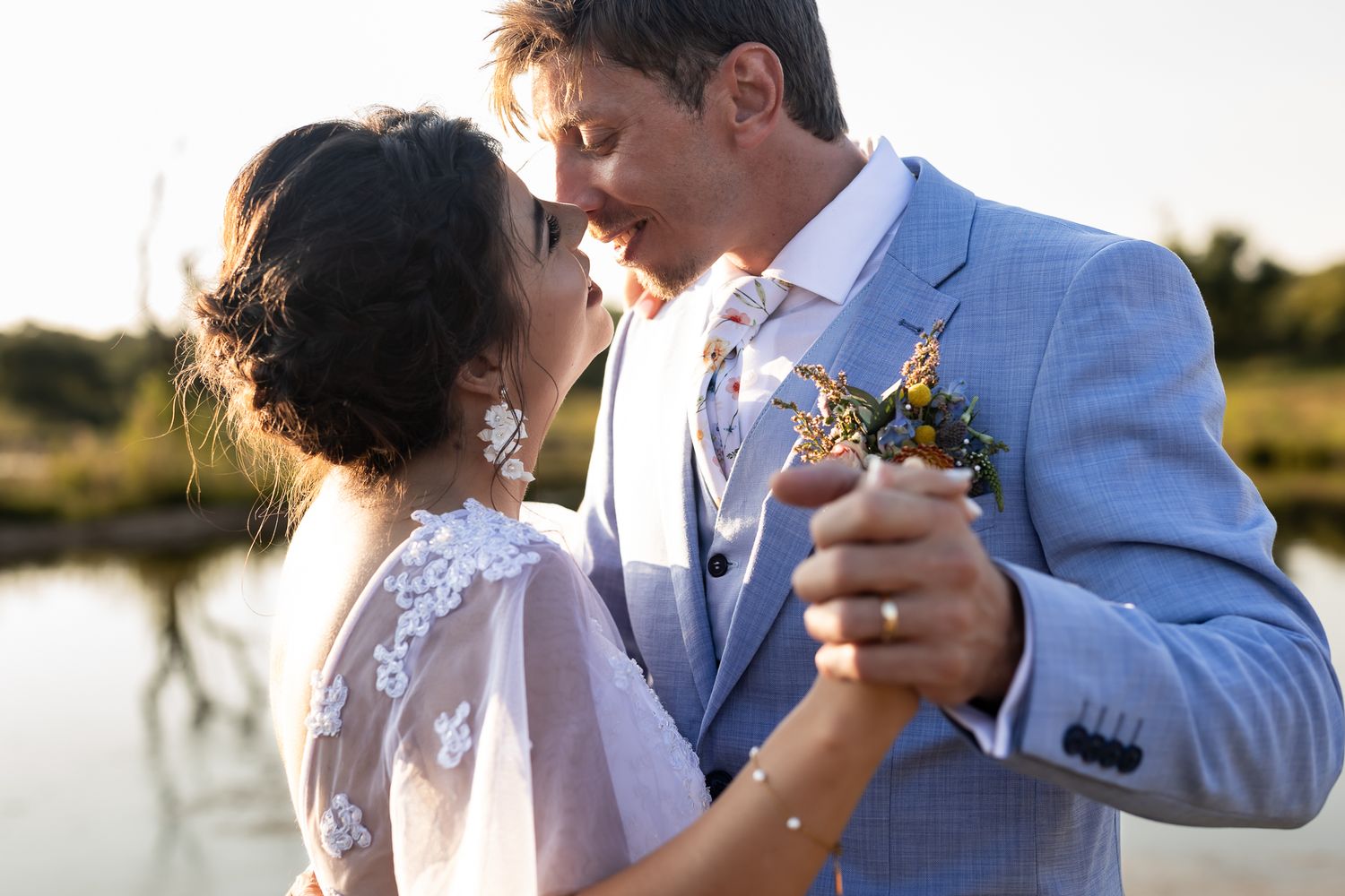 A couple dances together in formal attire by a lake during golden hour.