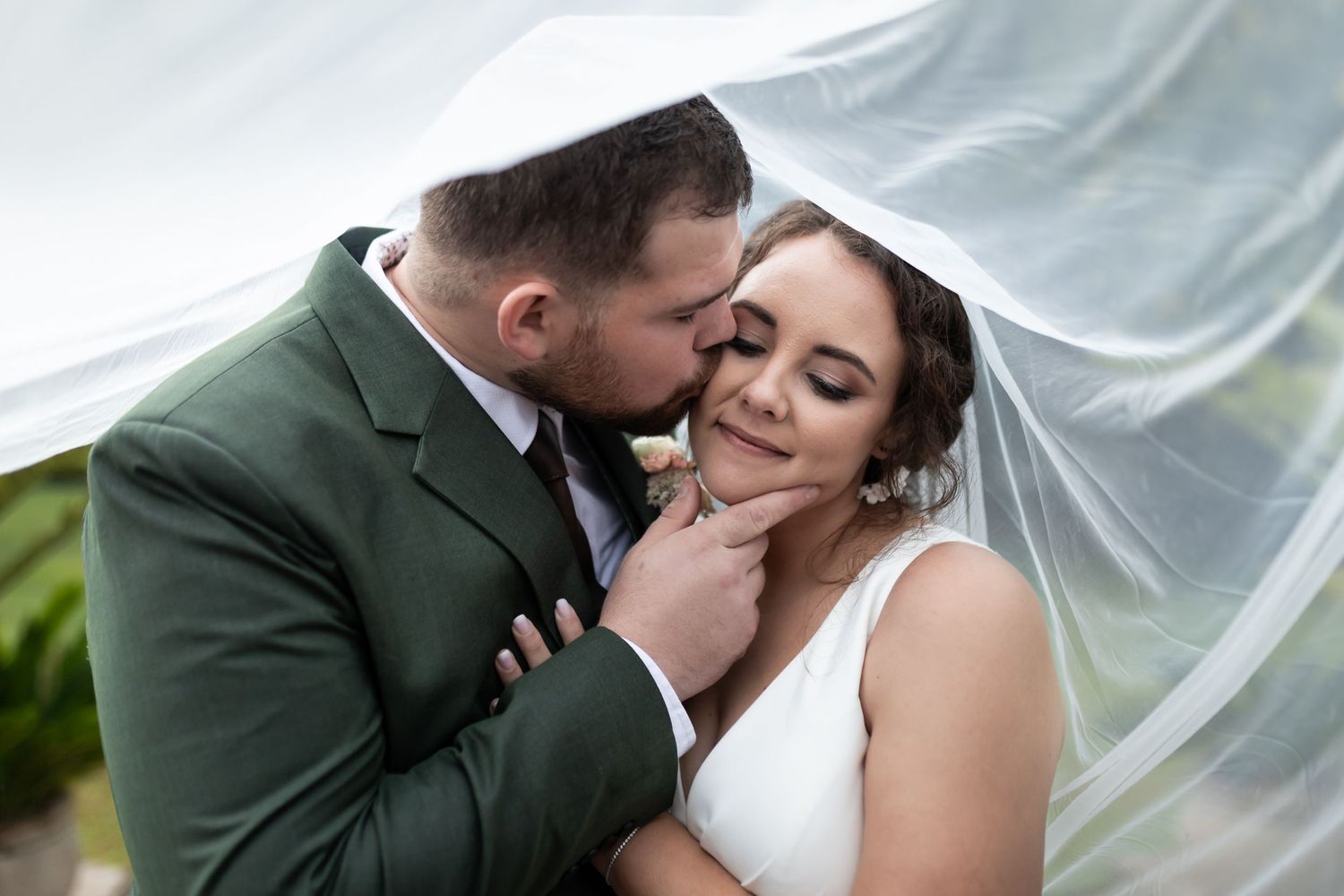 Tender moment captured under flowing veil with soft natural lighting.