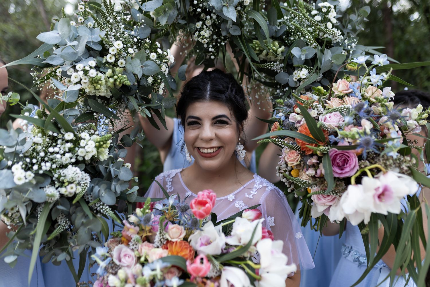 A bride surrounded by floral arrangements smiles during outdoor wedding photography.