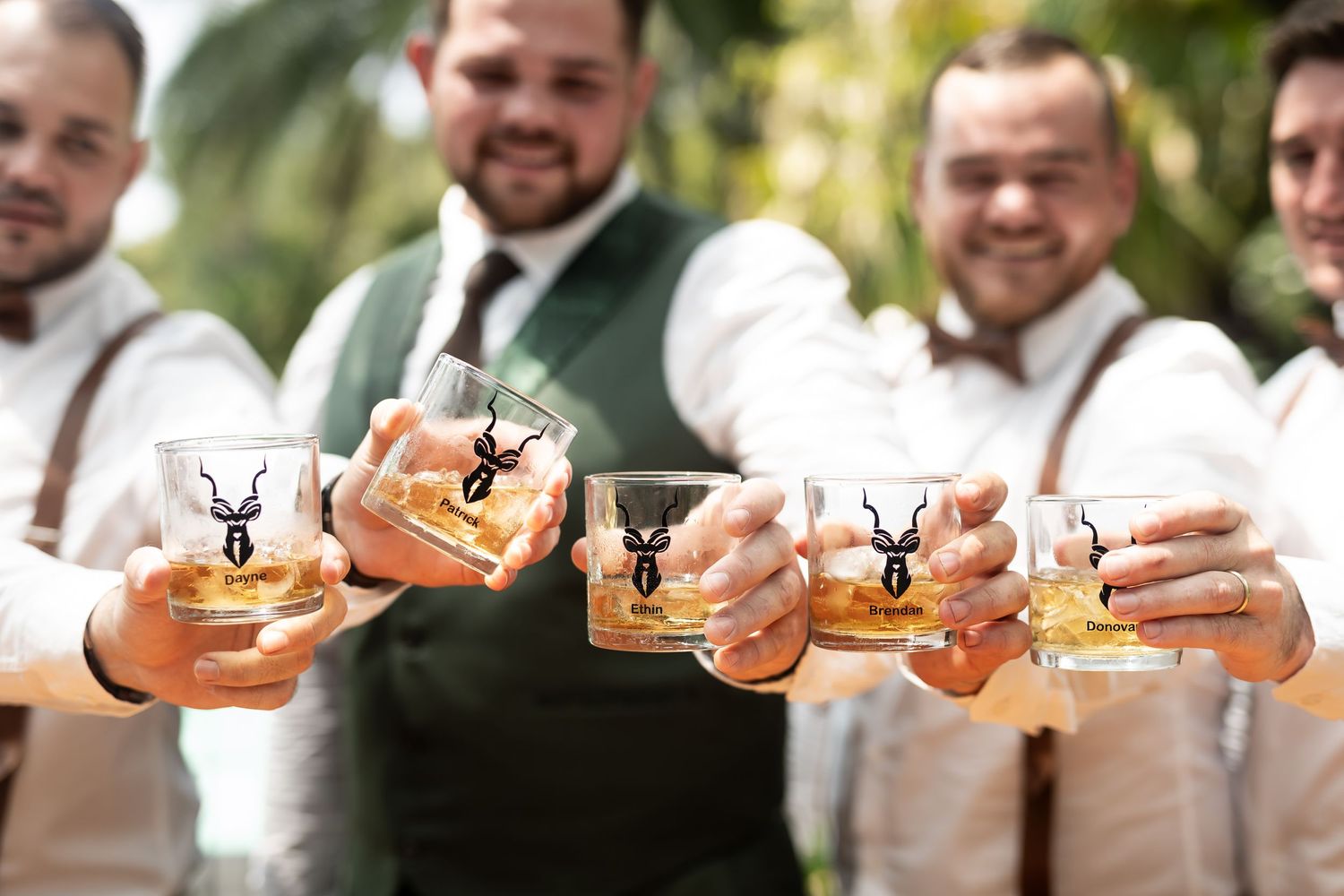 Closeup of groomsmen clinking glasses together in a celebratory toast outdoors.