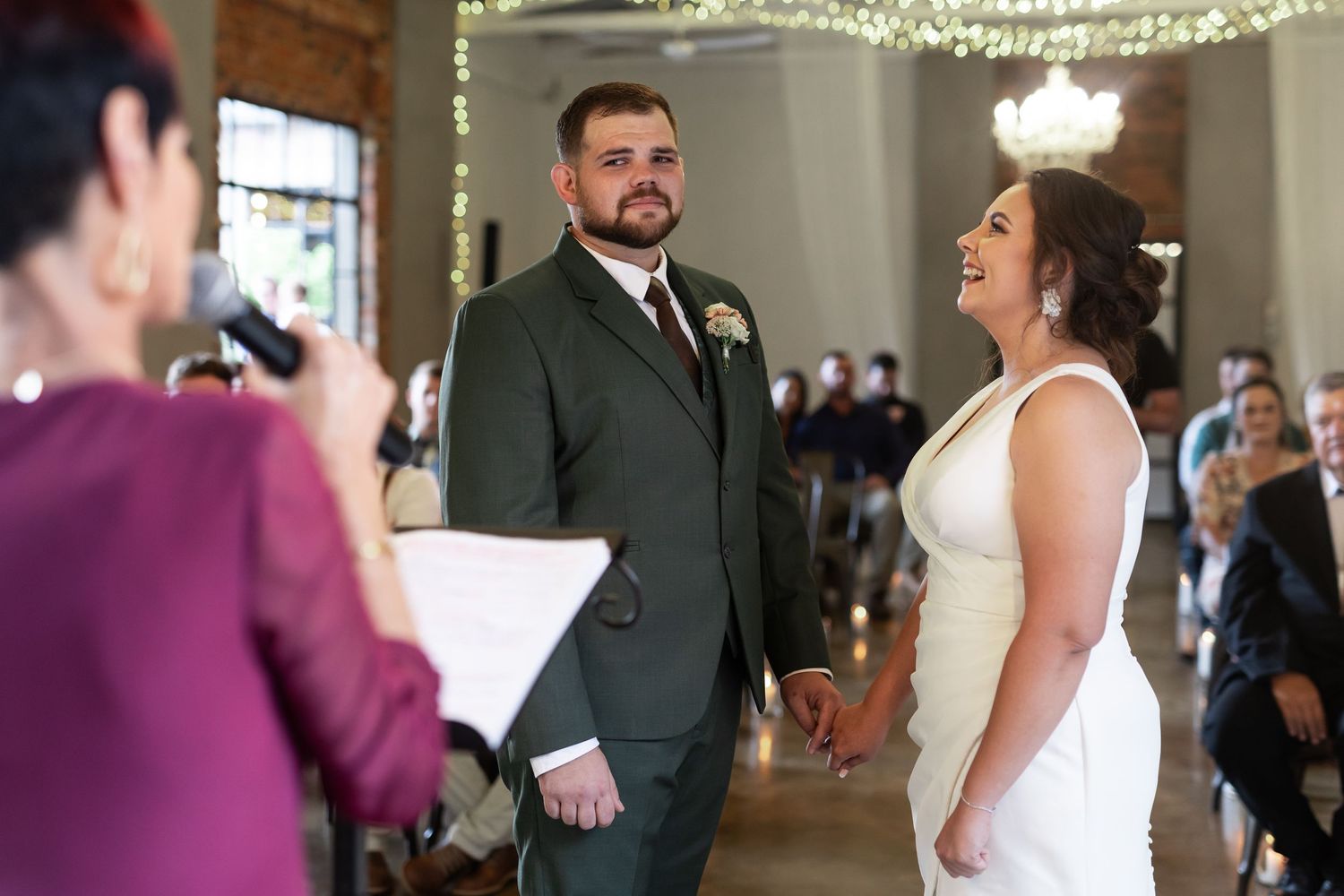 A couple exchanges vows during their wedding ceremony in an elegant venue with string lights.