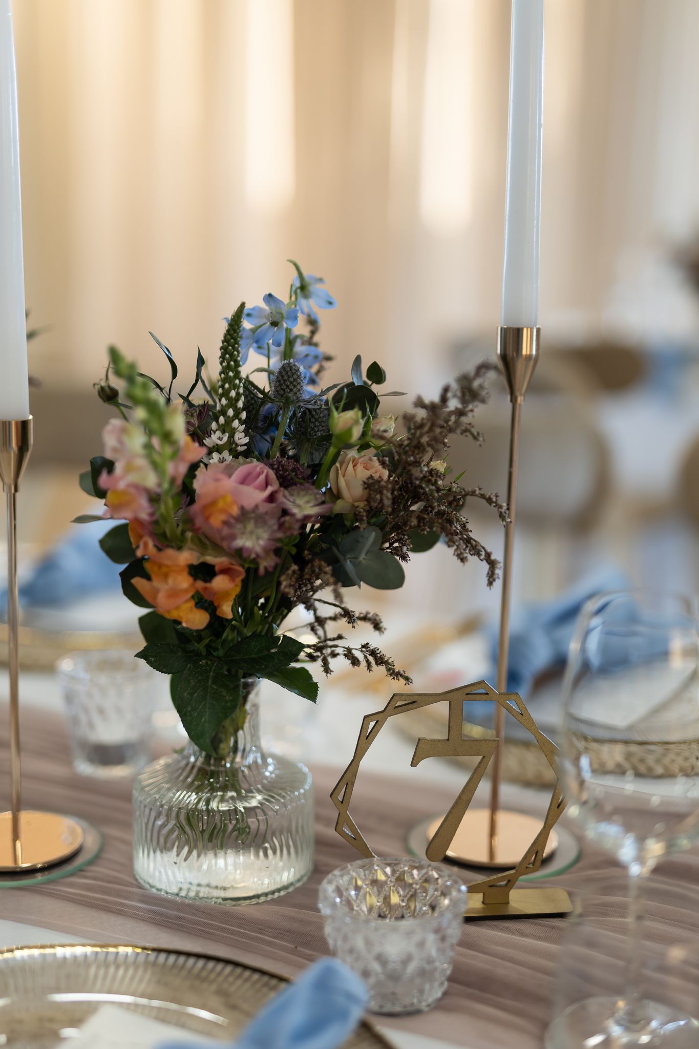 Delicate floral centerpiece with pink and blue blooms next to white taper candles.