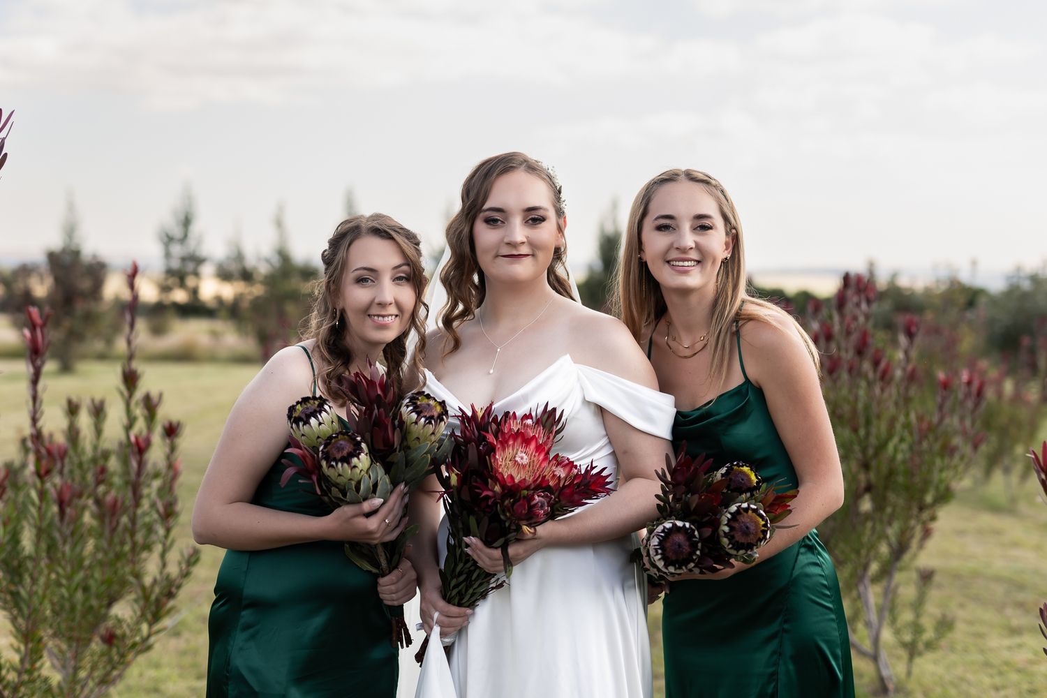 Wedding party poses outdoors with burgundy bouquets against natural landscape.