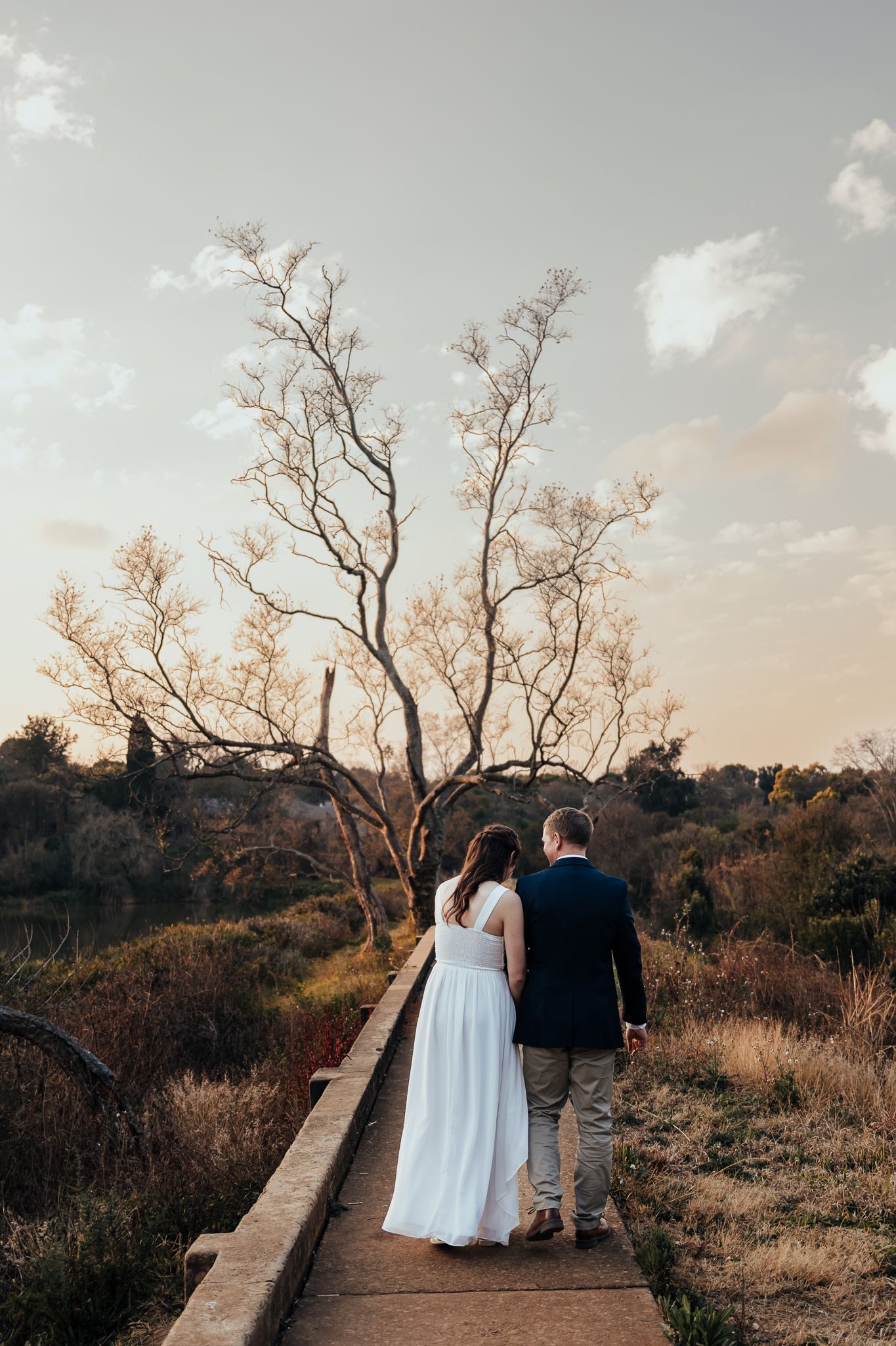 Couple walking together on dirt path through nature during golden hour wedding photography.