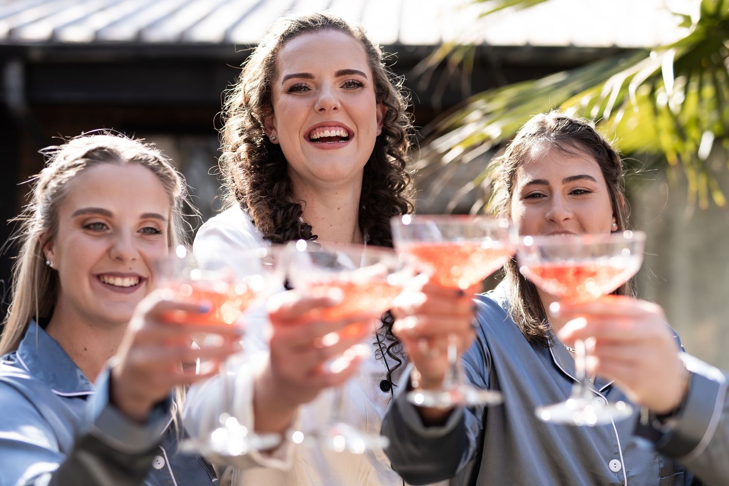 Three people enjoying cocktails together raise their martini glasses in a celebratory toast outdoors.