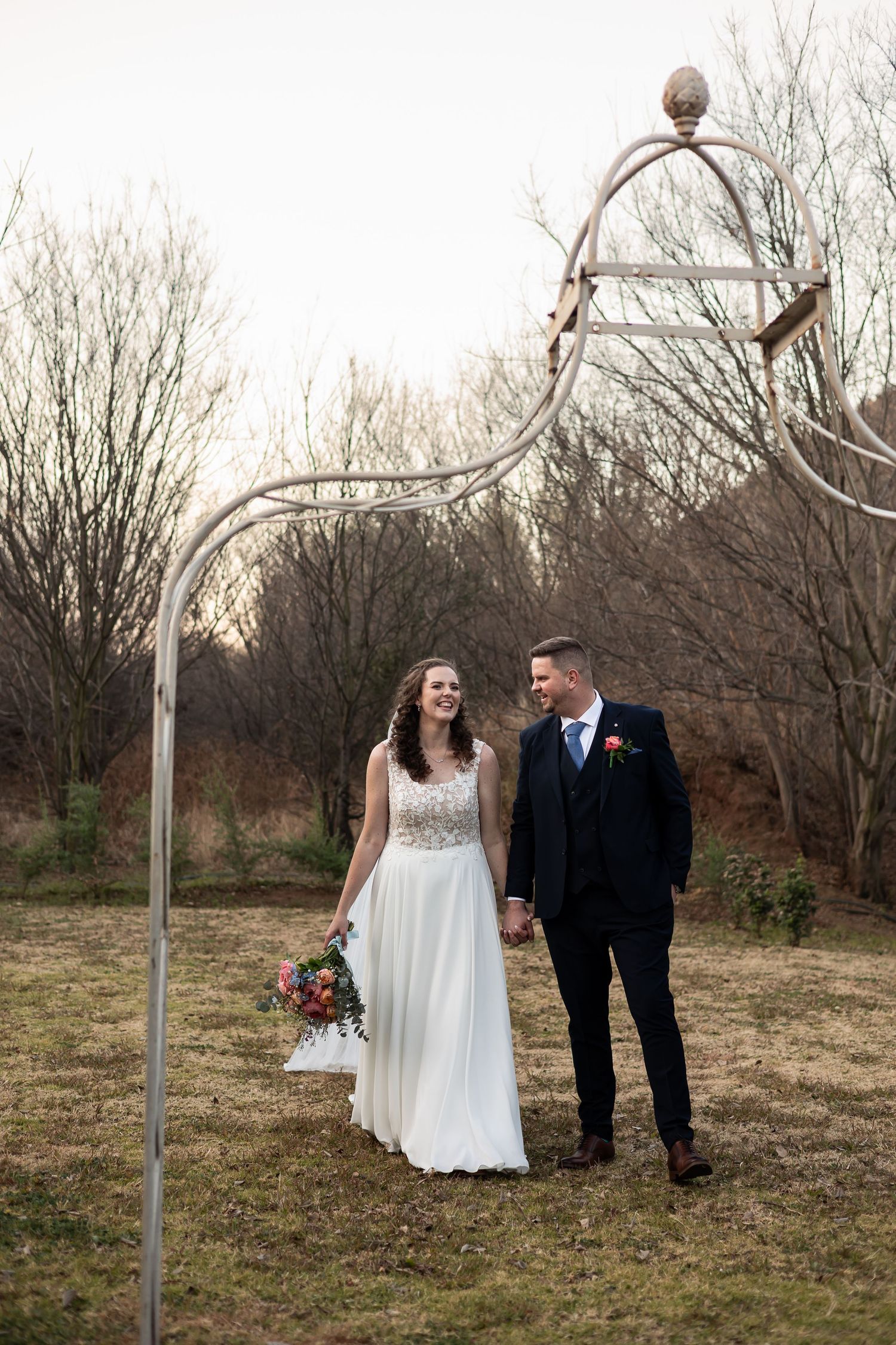 A bride and groom sharing a romantic moment in a natural outdoor setting with bare trees in the background.