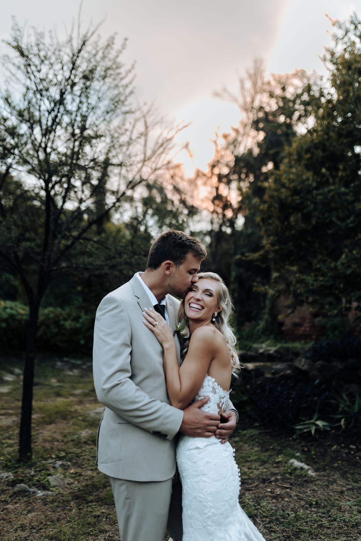 Romantic sunset wedding portrait in garden with light gray suit and lace gown.