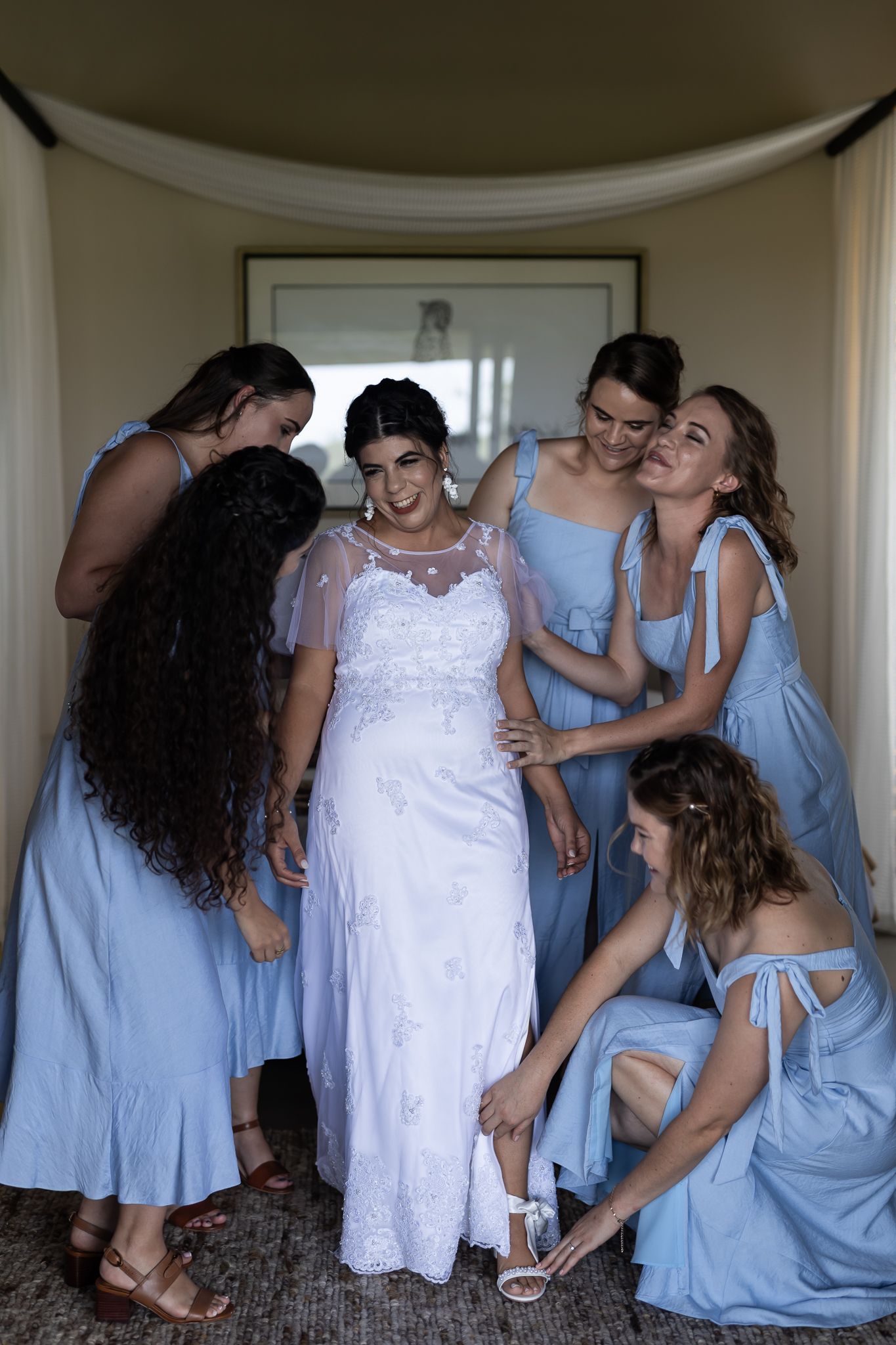 A wedding party shares a joyful moment as bridesmaids in blue dresses gather around the bride.