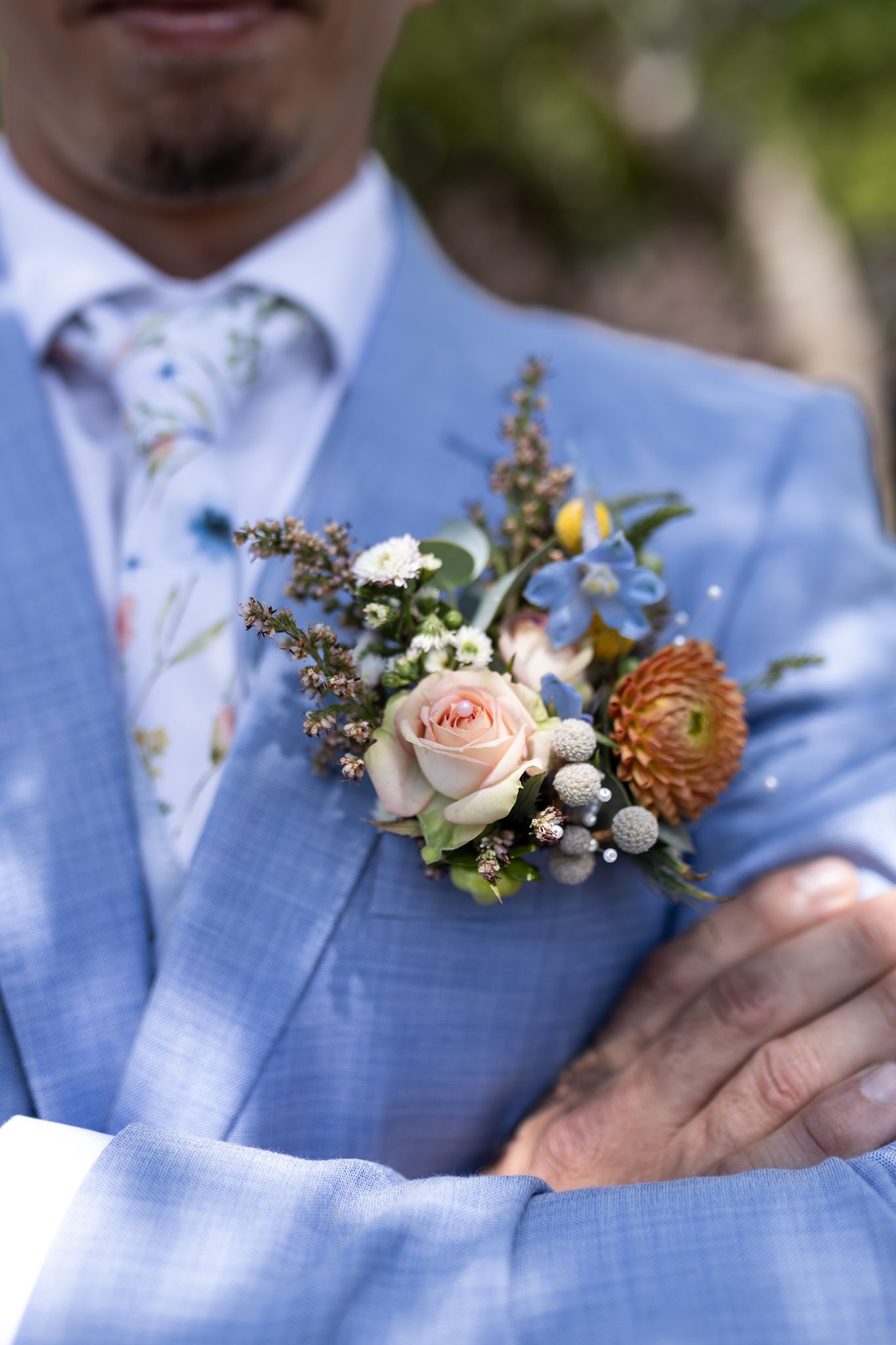 Close-up of boutonniere with pink rose and orange flowers on light blue suit jacket.