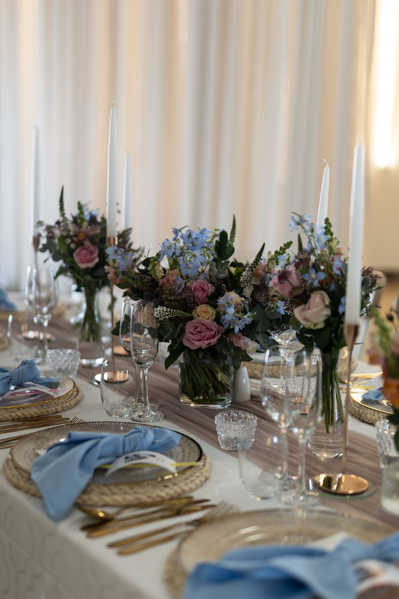 Elegant wedding table setting with floral centerpieces, blue napkins, and gold charger plates.