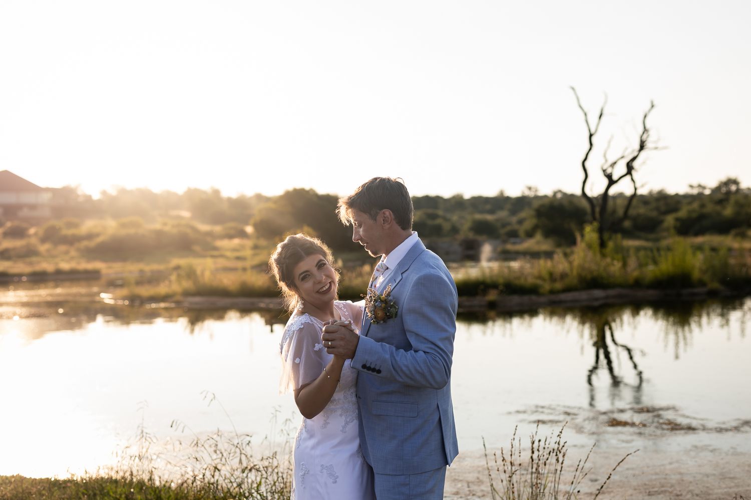 A couple shares an intimate moment at sunset by a serene lake with a bare tree branch reflection.