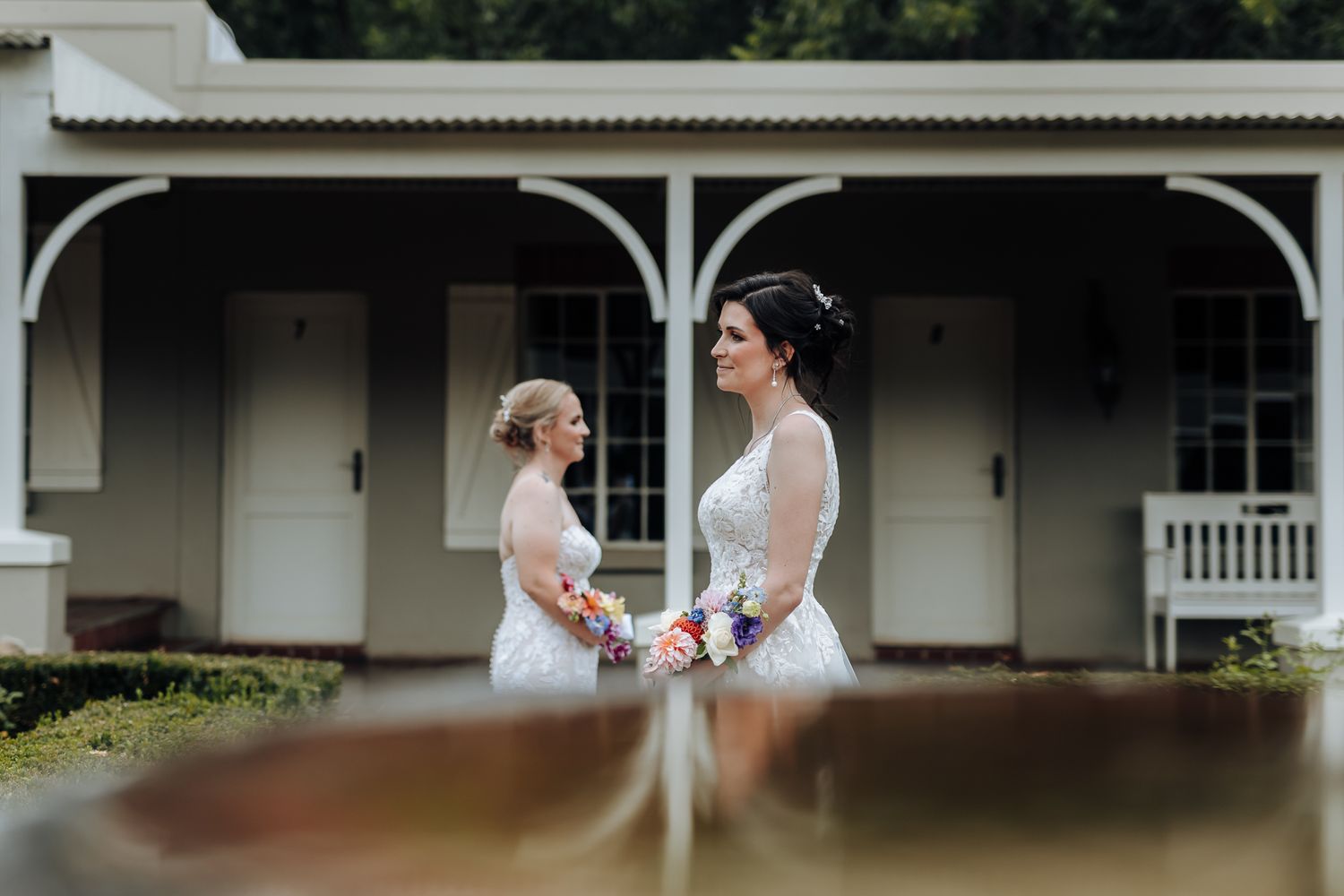 Couple in white wedding dresses hold hands in front of charming colonial style building.