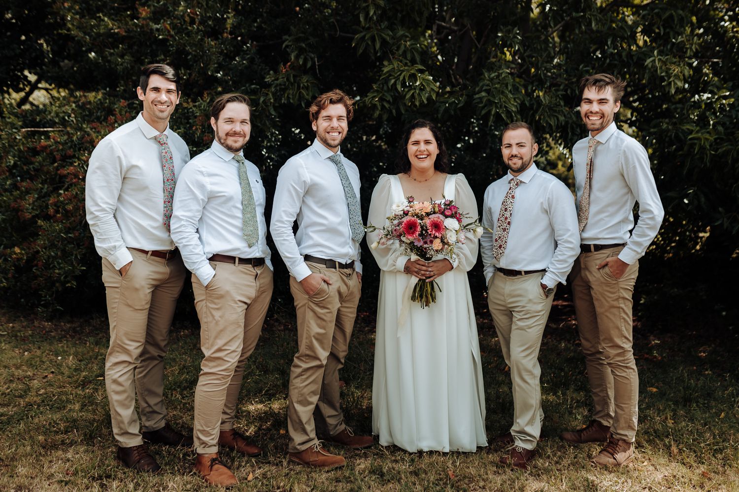 Wedding party in light colored shirts and khaki pants with bride in white dress.