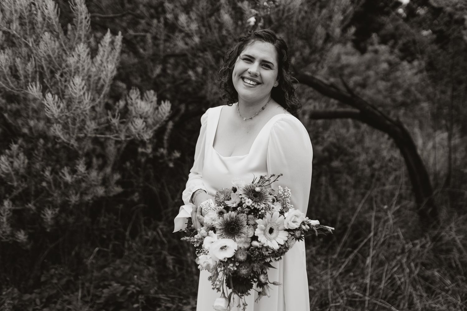 Black and white portrait of a bride holding a lush floral bouquet outdoors.