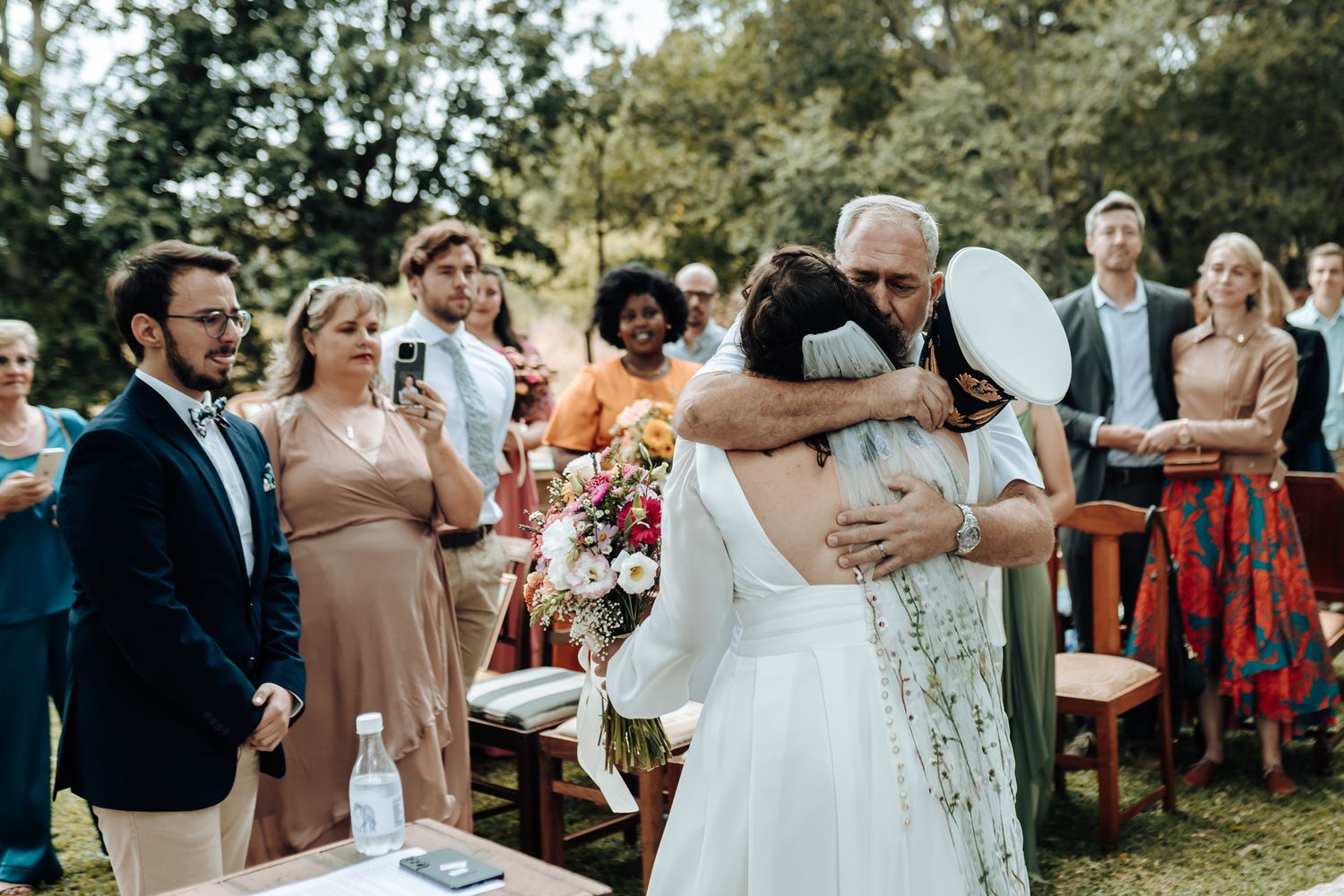 Emotional moment during outdoor wedding ceremony with guests watching.