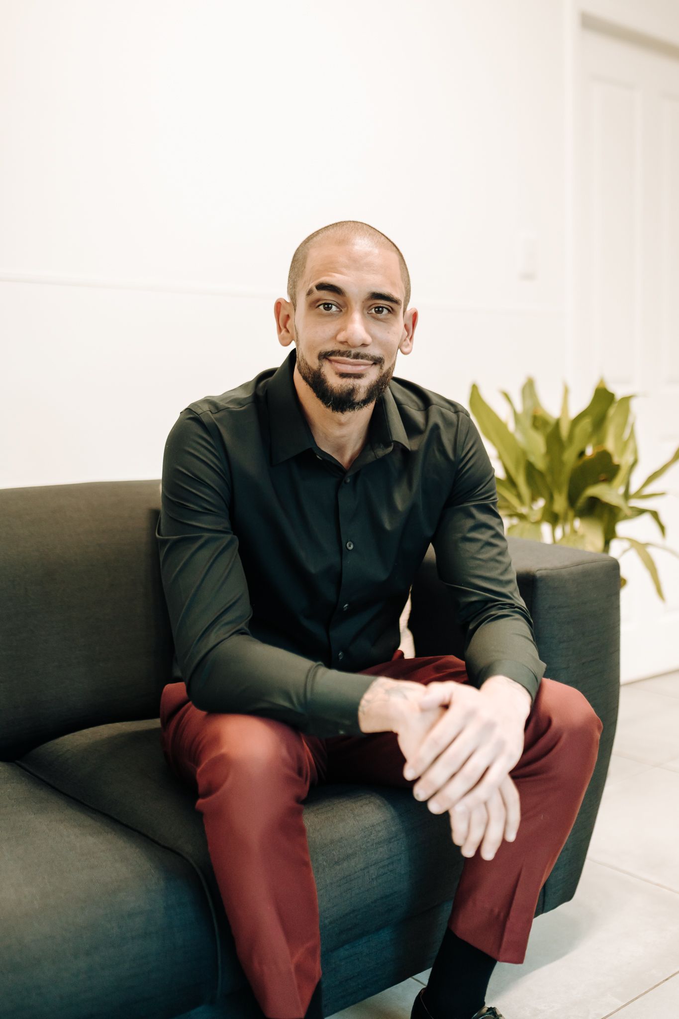 Person in black shirt and burgundy pants sitting on grey couch in modern interior.