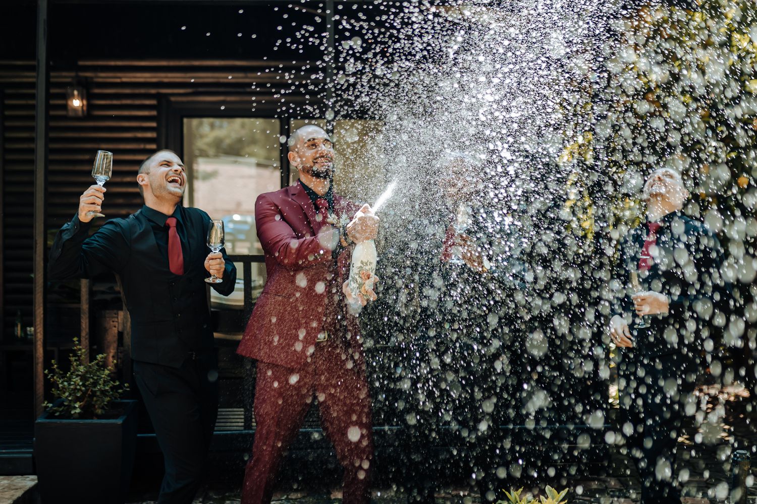Celebratory moment with champagne spraying outdoors against wooden backdrop.