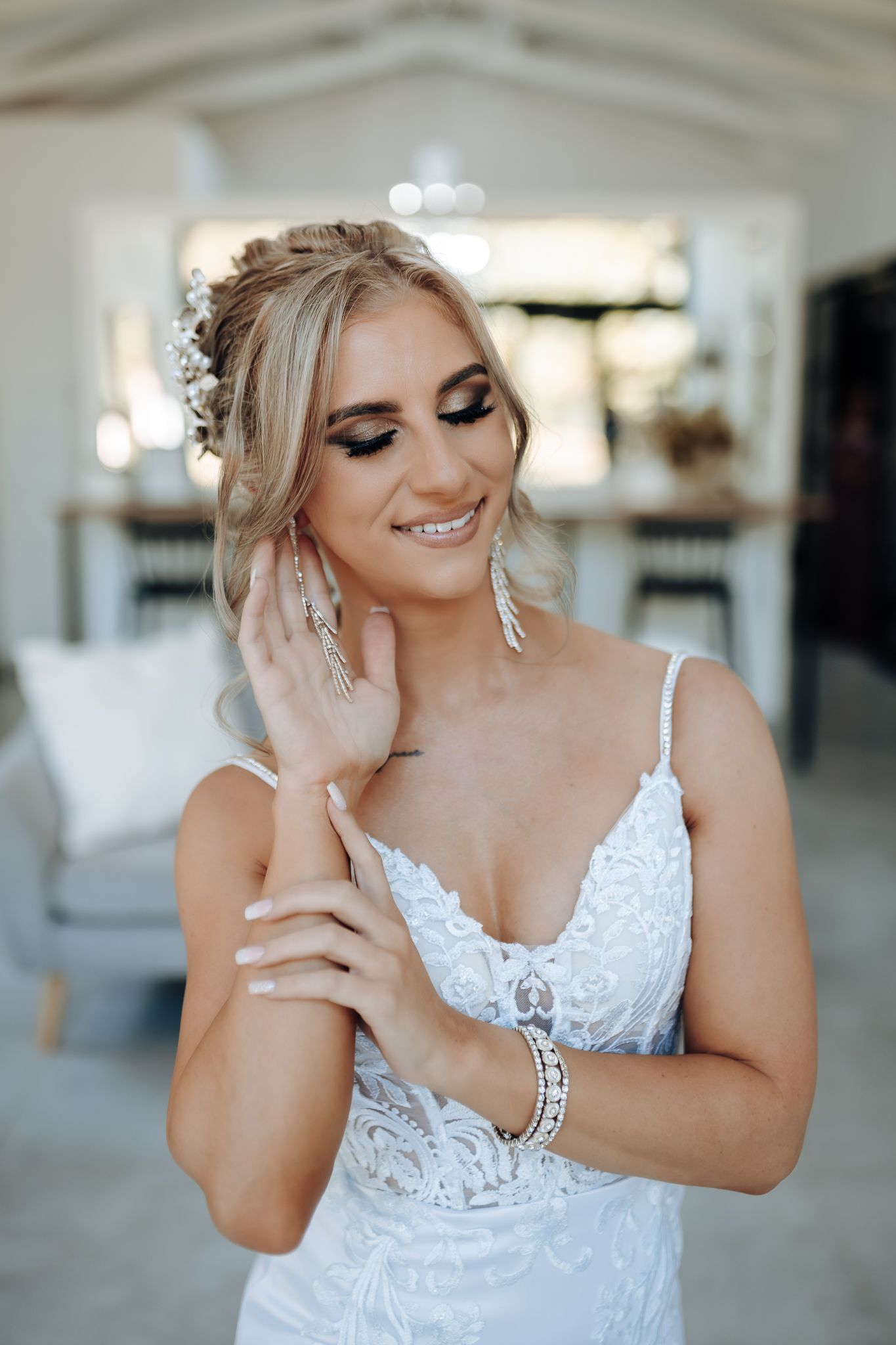Close up of person in lace wedding dress smiling while touching elegant floral hair accessories.