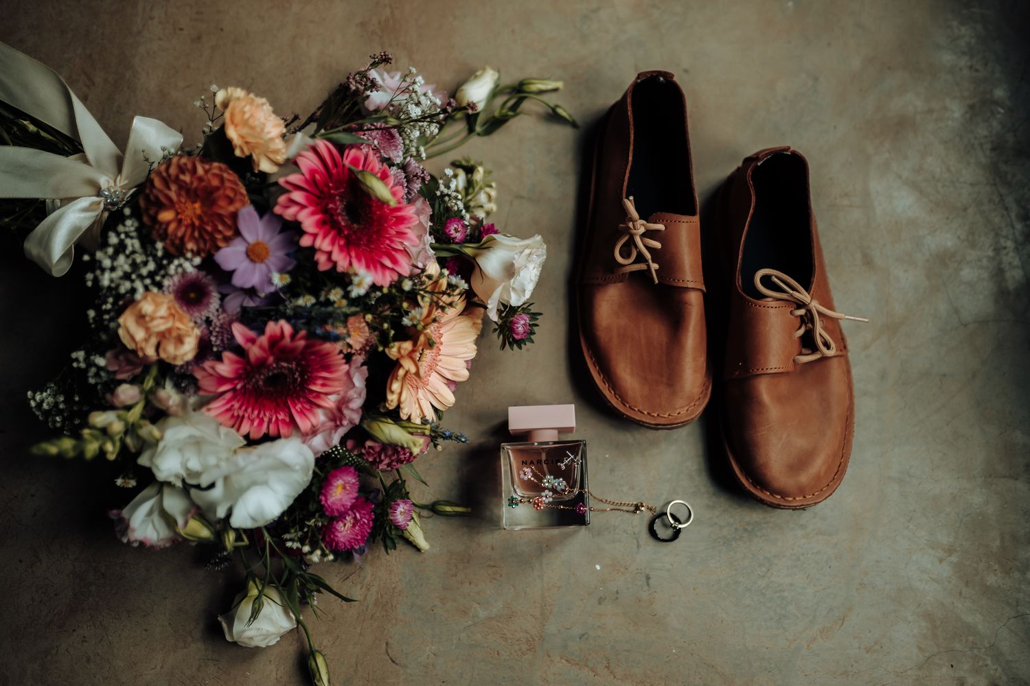 Wedding details featuring brown leather shoes and vibrant floral bouquet with pink gerbera daisies.