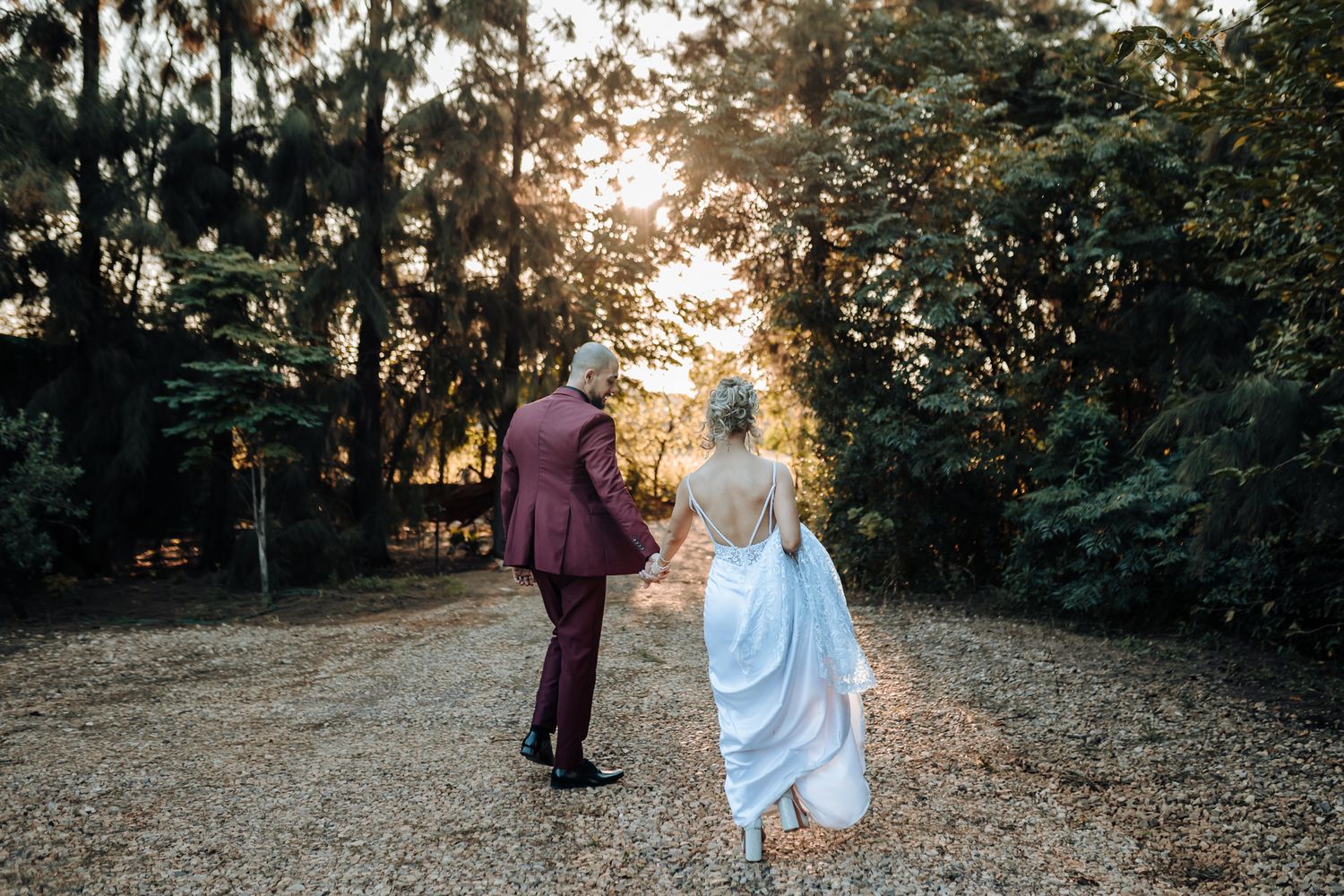 Wedding couple walking into sunset on garden path.