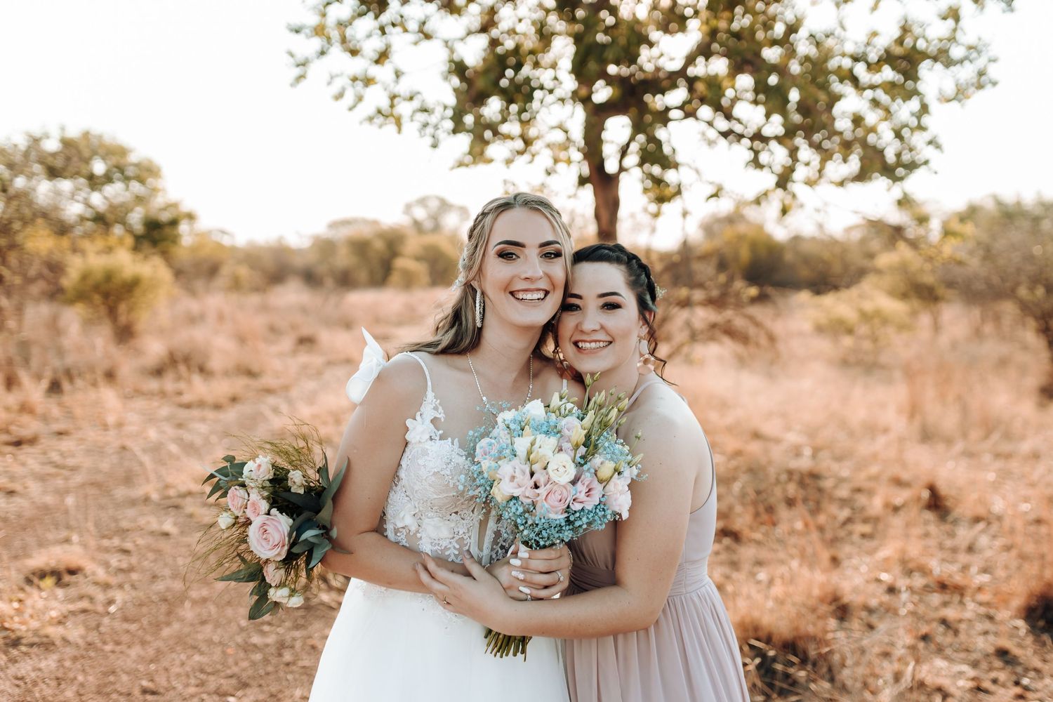 Wedding portrait with bride and bridesmaid holding bouquets in sunset landscape.
