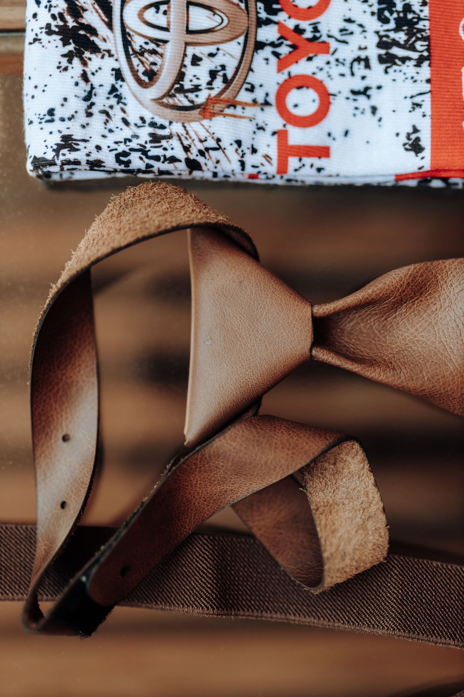 Detailed shot of a brown leather bow tie and suspenders against a dark surface.