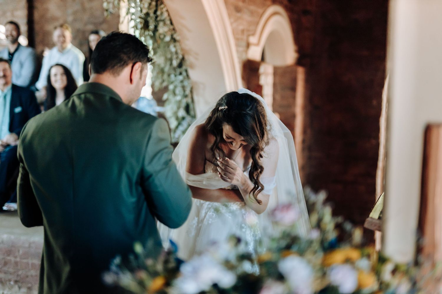Emotional moment during wedding ceremony as couple wipes tears under stone archway.