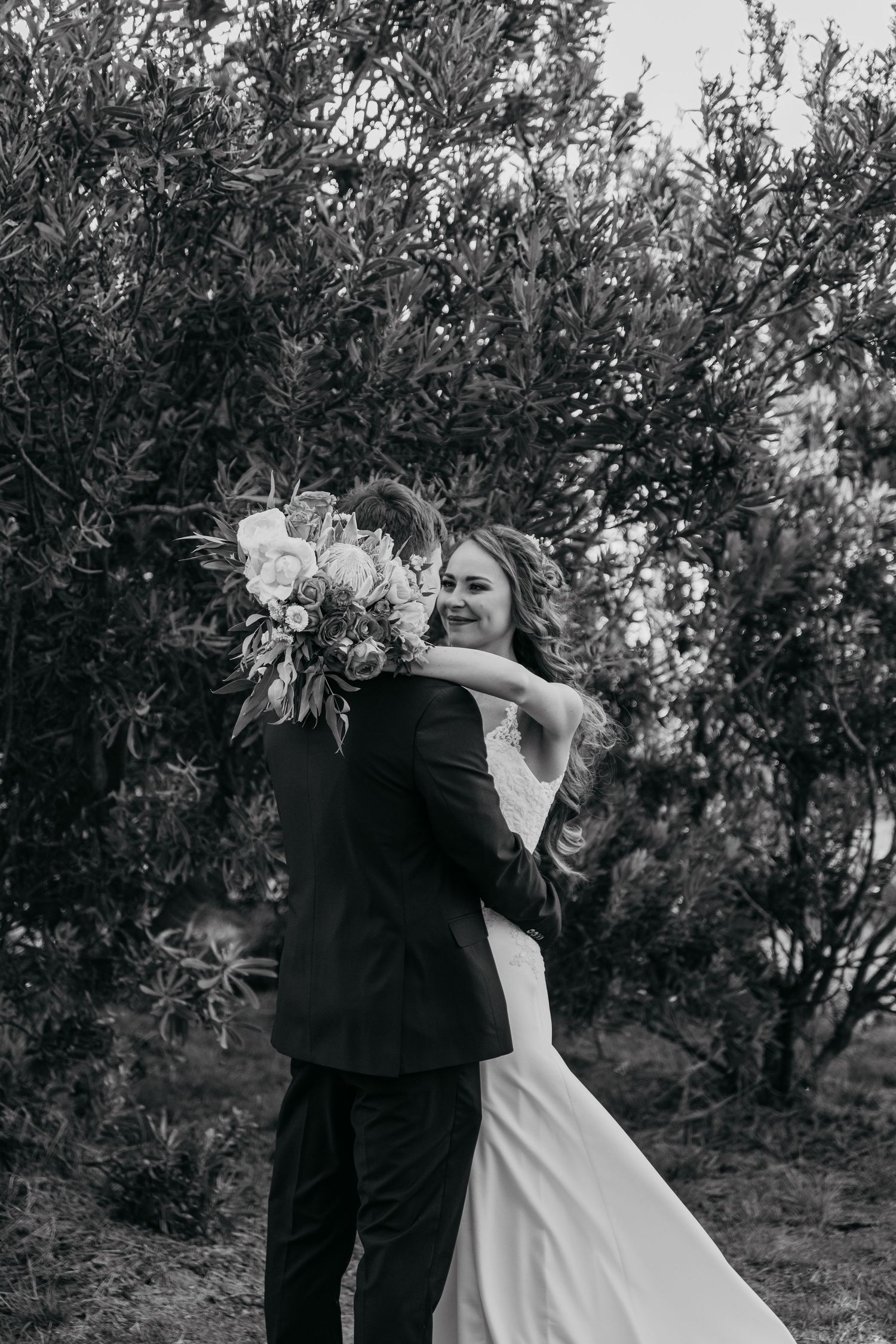 A romantic black and white wedding photo shows an embrace against a leafy backdrop.