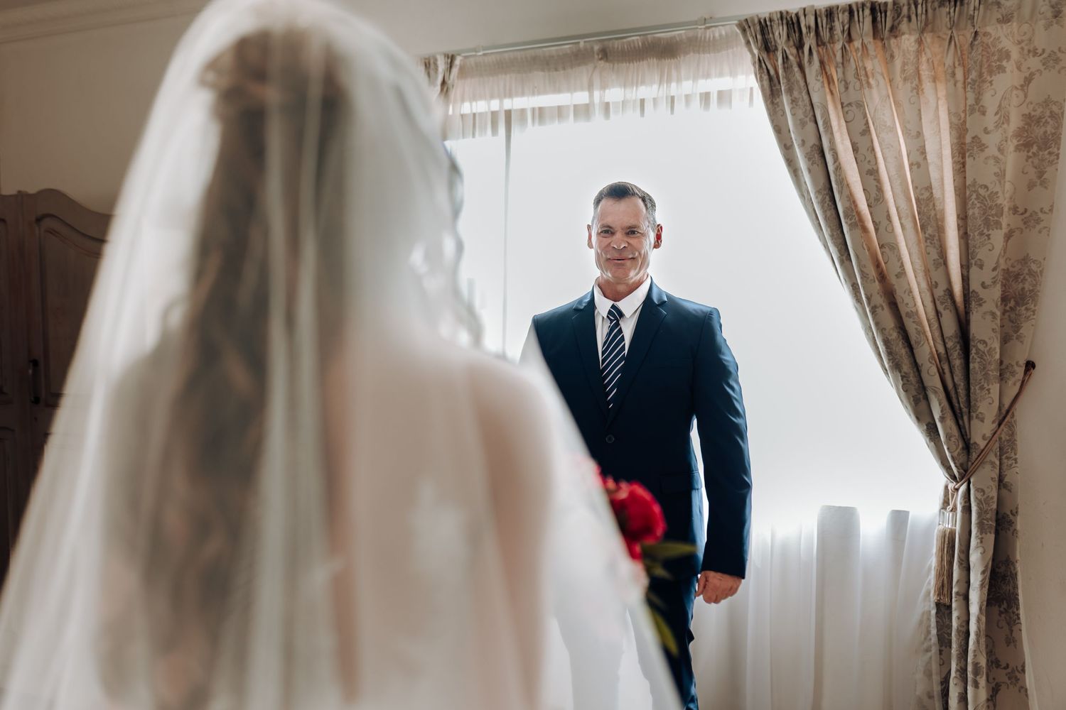 First look moment between bride and groom by window in elegant room.