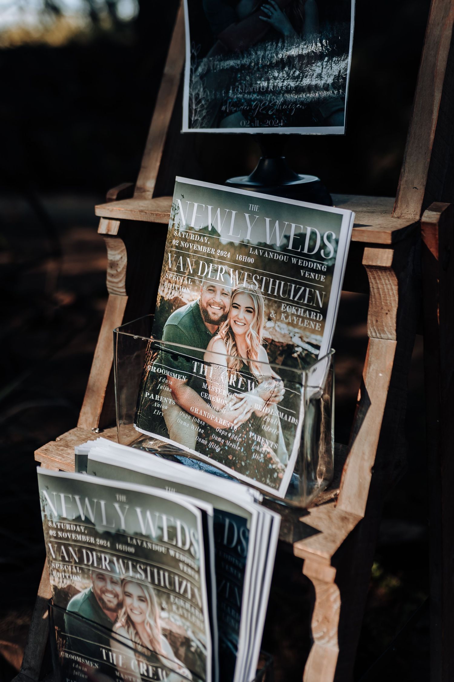 Wedding magazines displayed on rustic wooden stand at outdoor venue.