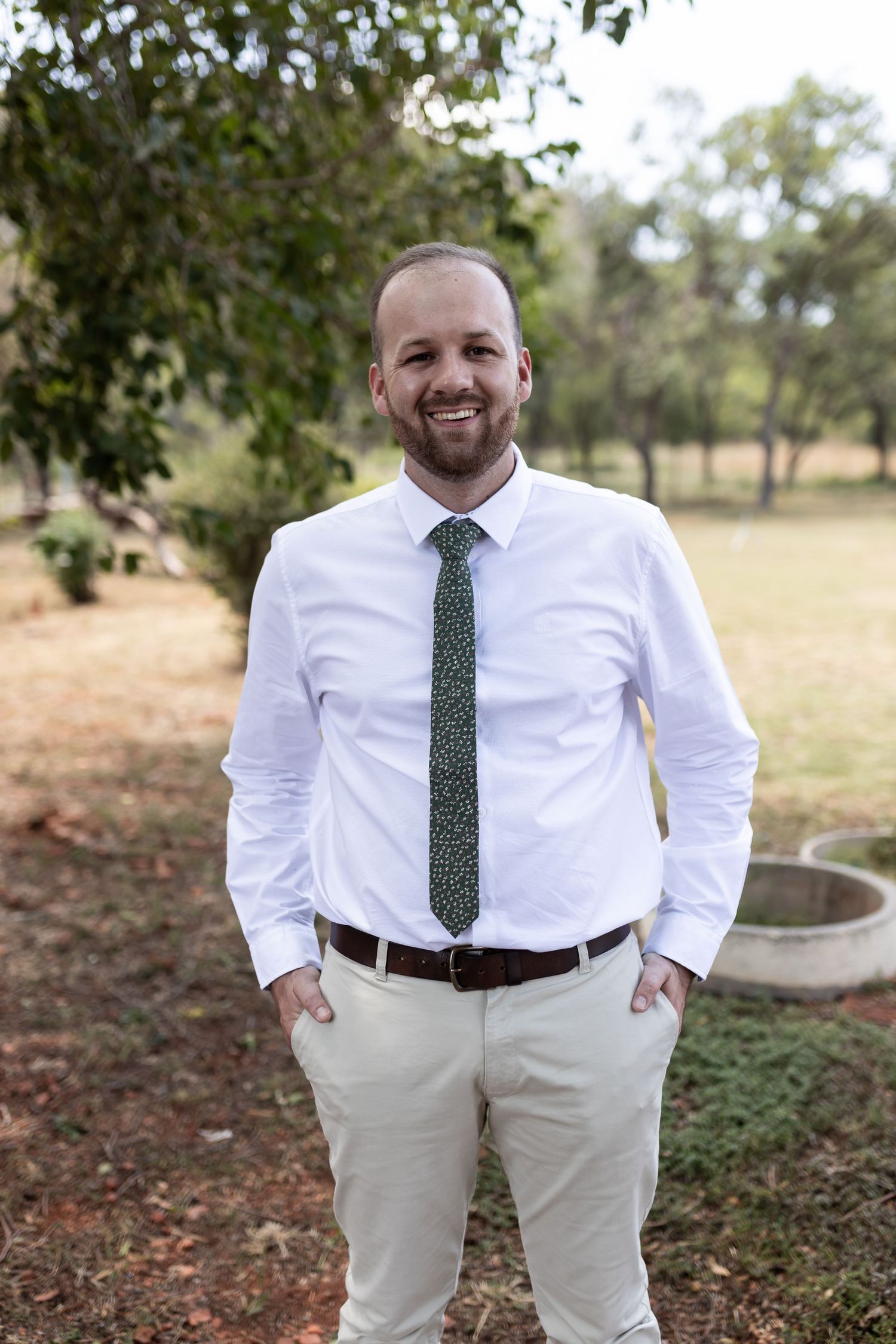 Wedding party member wearing white shirt and green tie poses in outdoor setting.