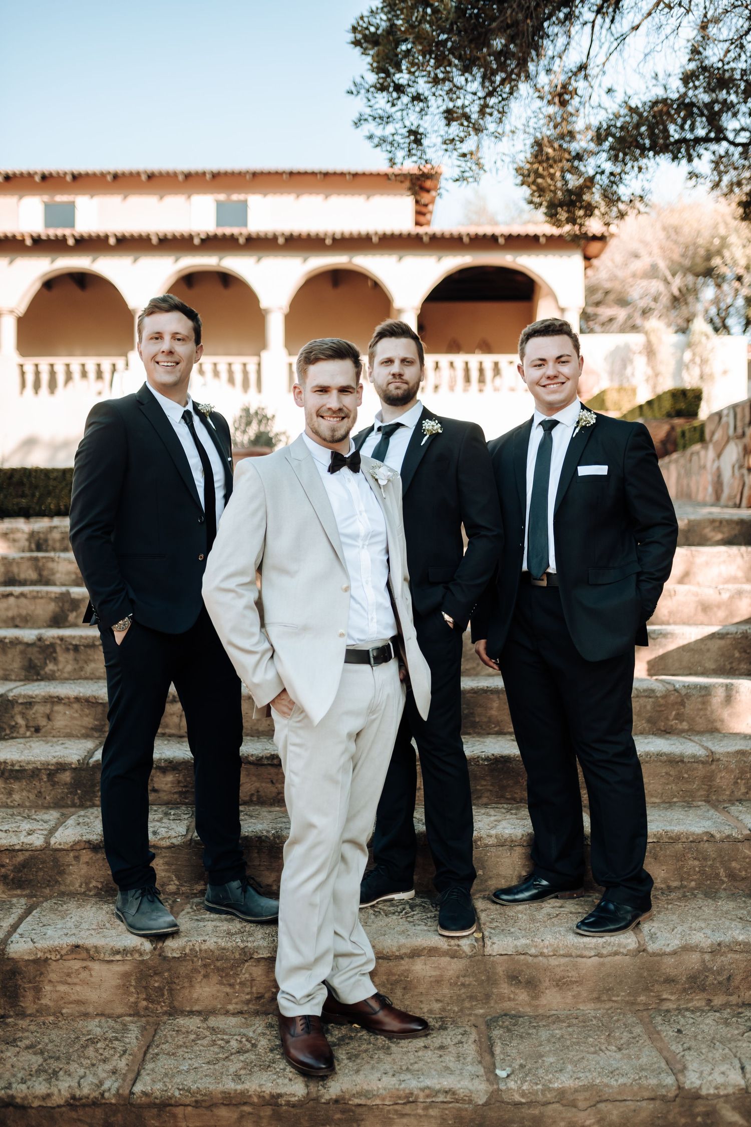 Groomsmen in black suits with one in white pose on Mediterranean-style stone steps.