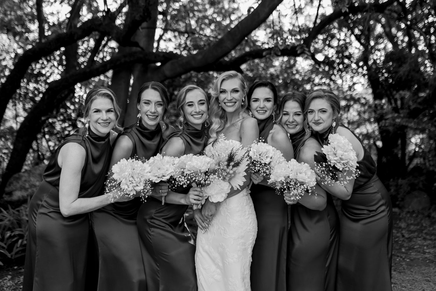 Black and white portrait of bridal party with bouquets under tree branches.