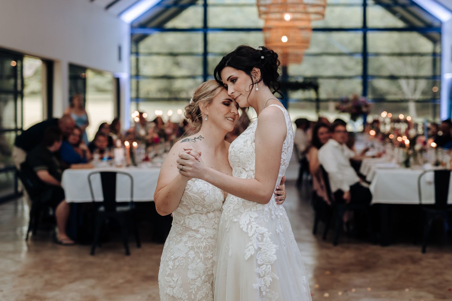 A gentle embrace during a wedding reception with guests seated at tables in the background.