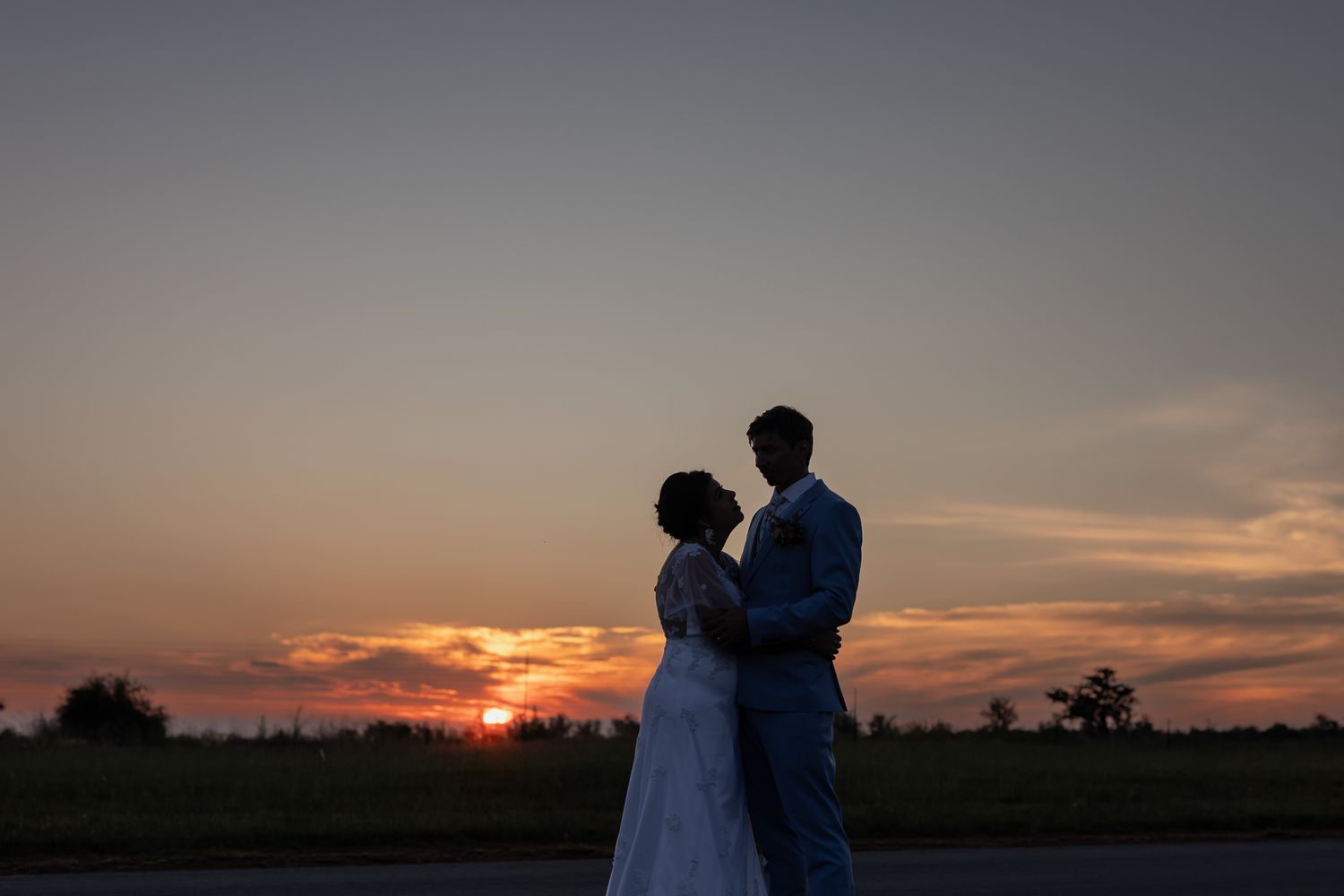 Silhouette of wedding couple embracing against dramatic sunset sky.