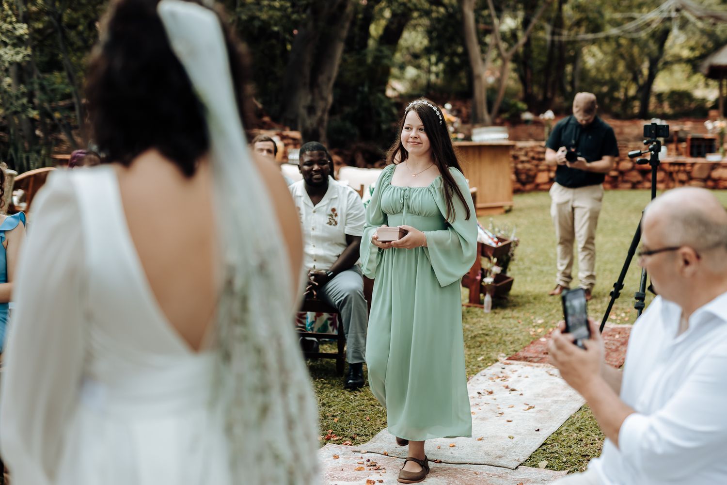 Bridesmaid in mint green dress walking down outdoor aisle during wedding ceremony.