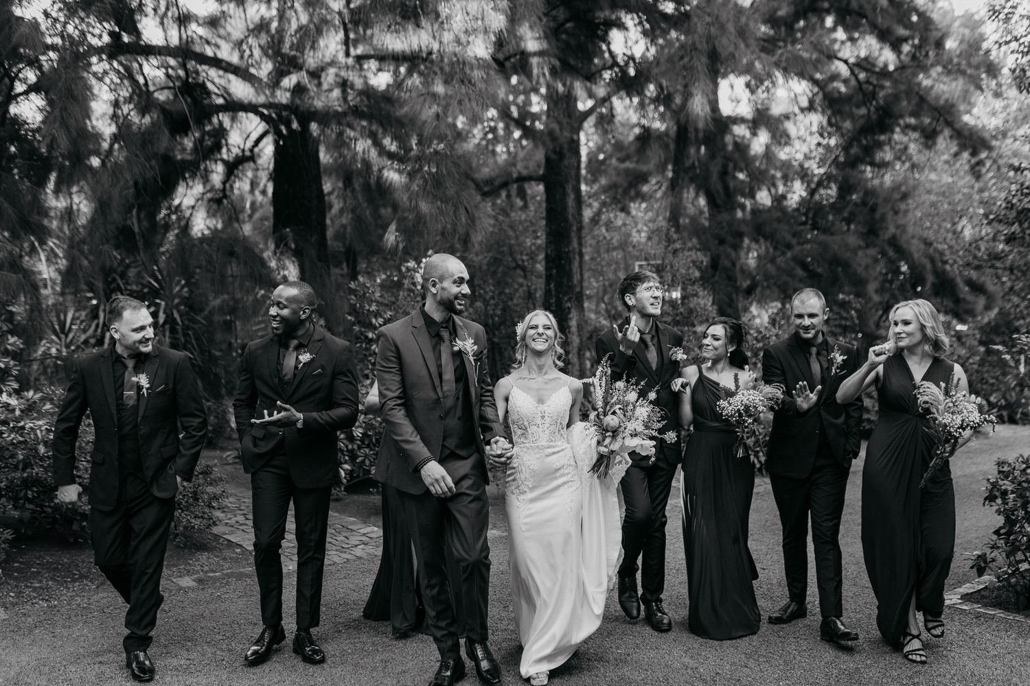 Wedding party walks and laughs together on outdoor path in black and white photograph.