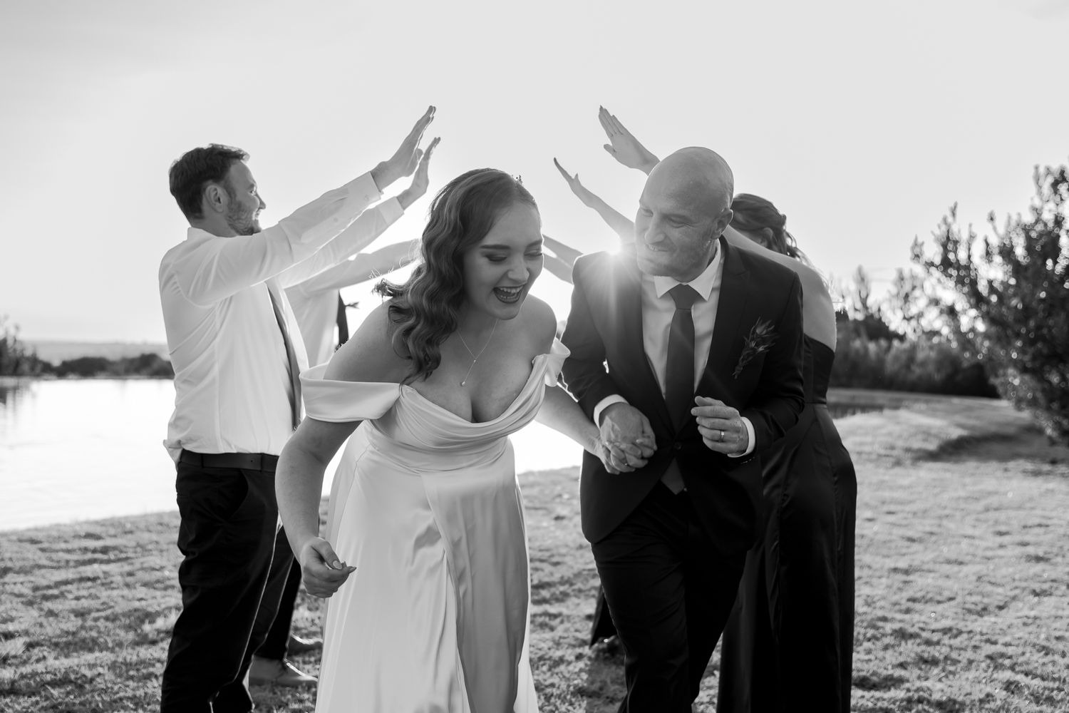 Black and white photo of wedding party celebrating with raised arms at sunset.